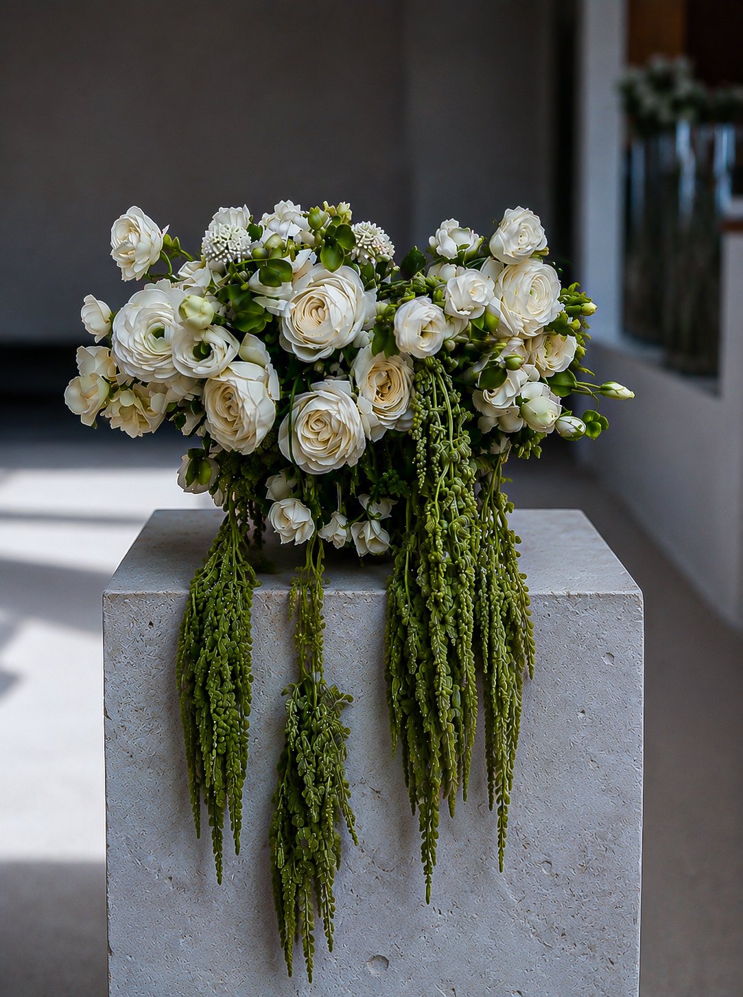 A bouquet of white roses and small white flowers with green cascading foliage on a white pedestal.
