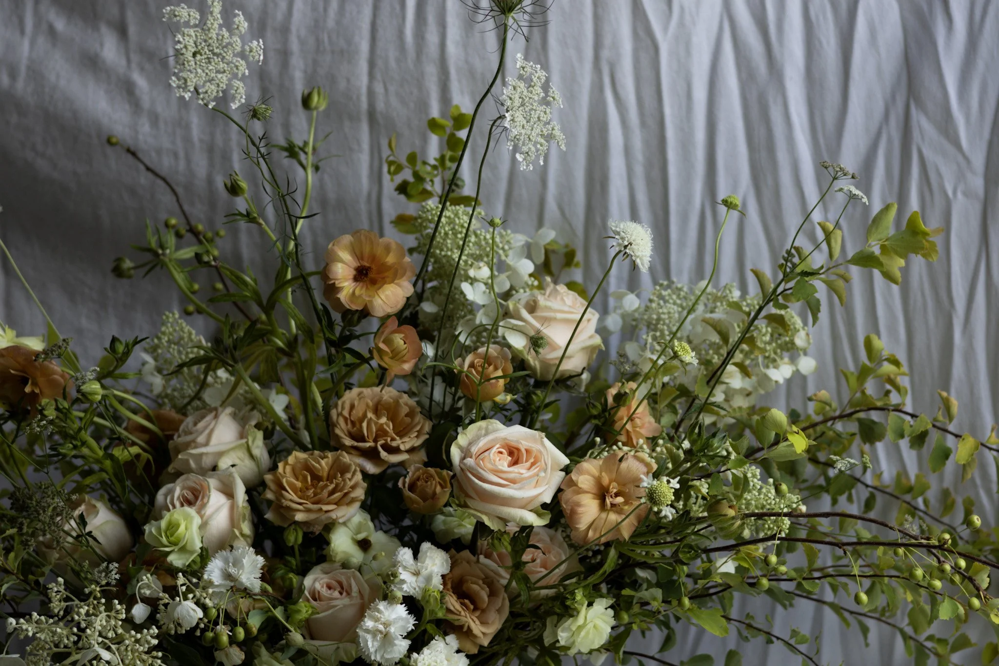 A large bouquet of mixed flowers including roses, carnations, and greenery arranged in front of a textured wall.