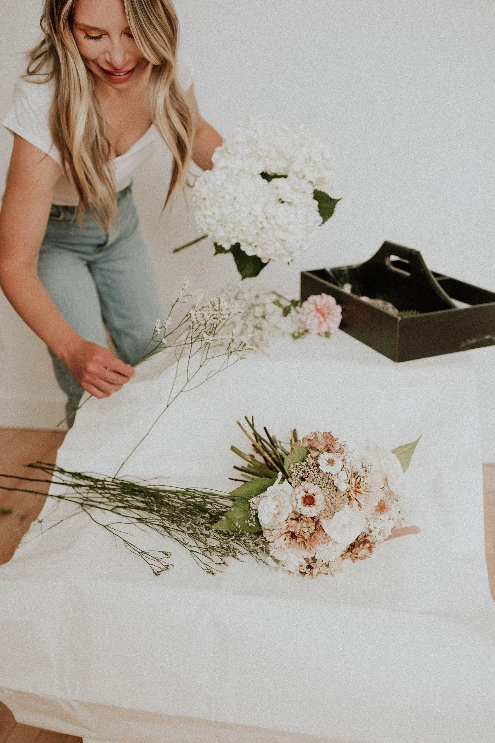 A woman arranging a bouquet of white and pink flowers on a white table.