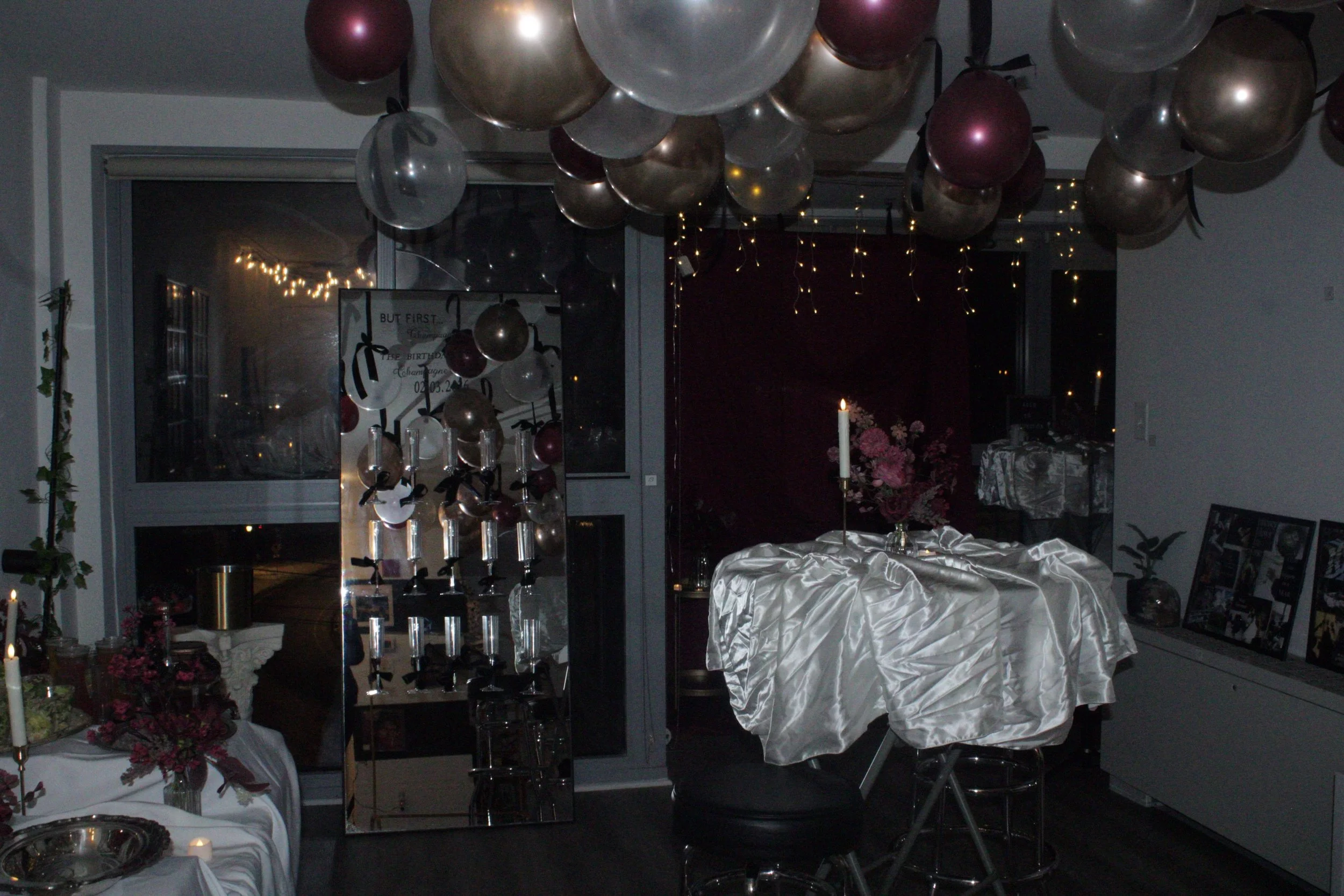 Decorated party room with balloons, string lights, candles, flowers, and framed photos.