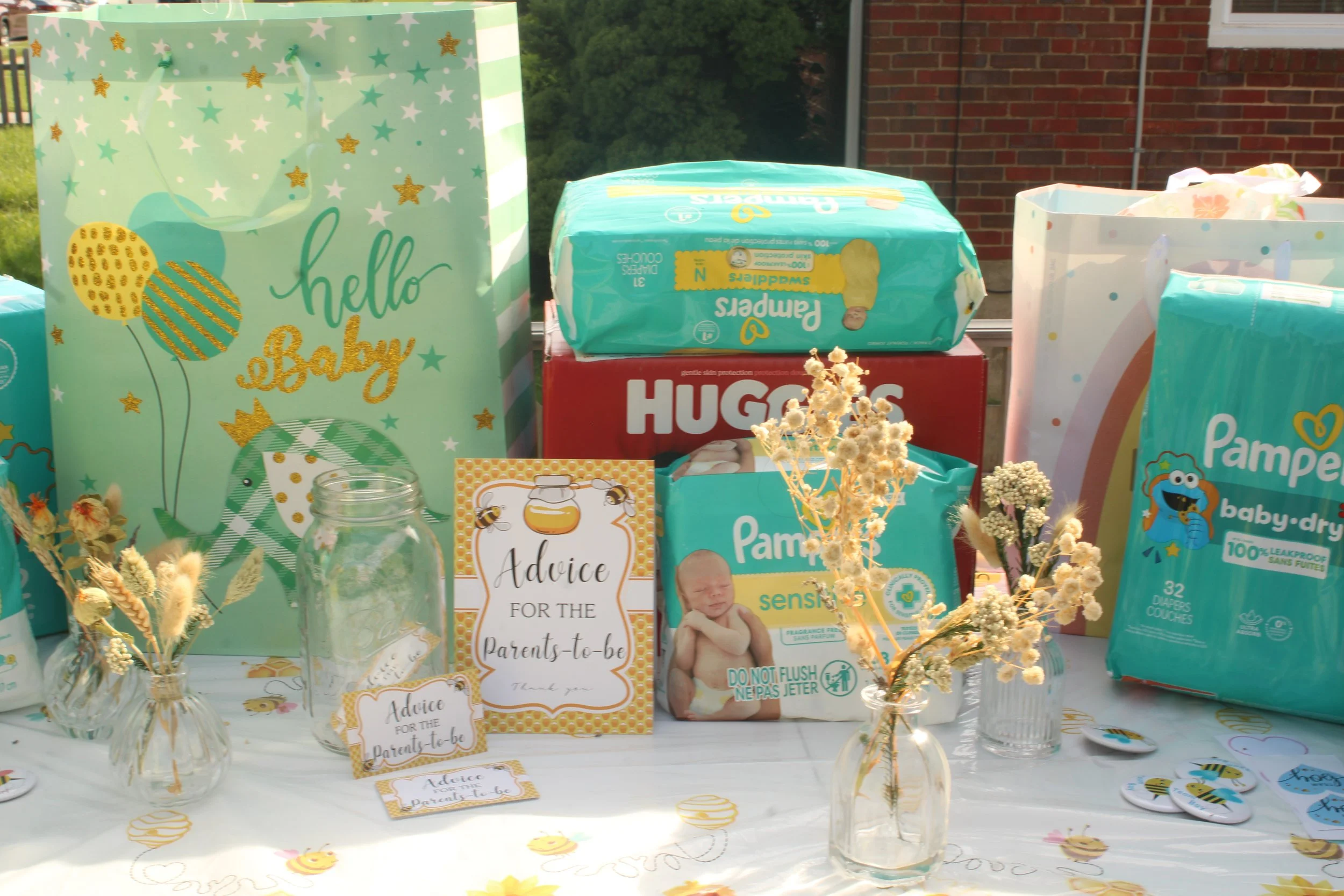 Diaper and baby essentials on display at a baby shower, including Pampers diapers, a Huggies box, advice cards for parents-to-be, and decorative vases with dried flowers.