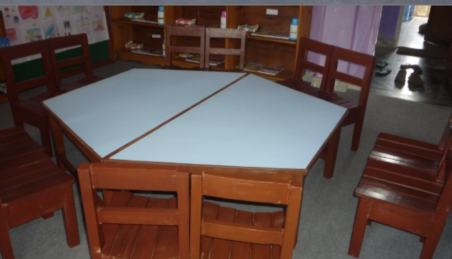 Classroom table with white top surrounded by wooden chairs in a classroom setting.