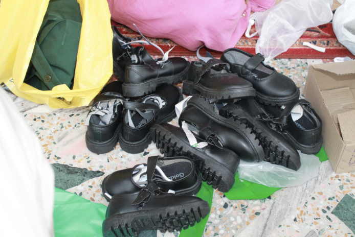 Several pairs of black shoes with thick, ridged soles arranged on the floor among shopping bags and packaging material.