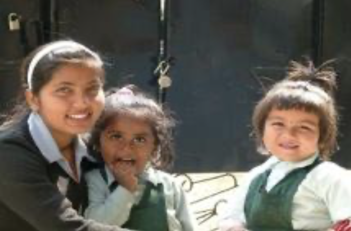 Three young girls in school uniforms smiling and posing for a photo indoors.