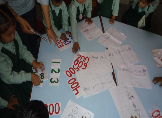 Children gathered around a table with papers, drawings, and number cards, engaged in a learning activity.