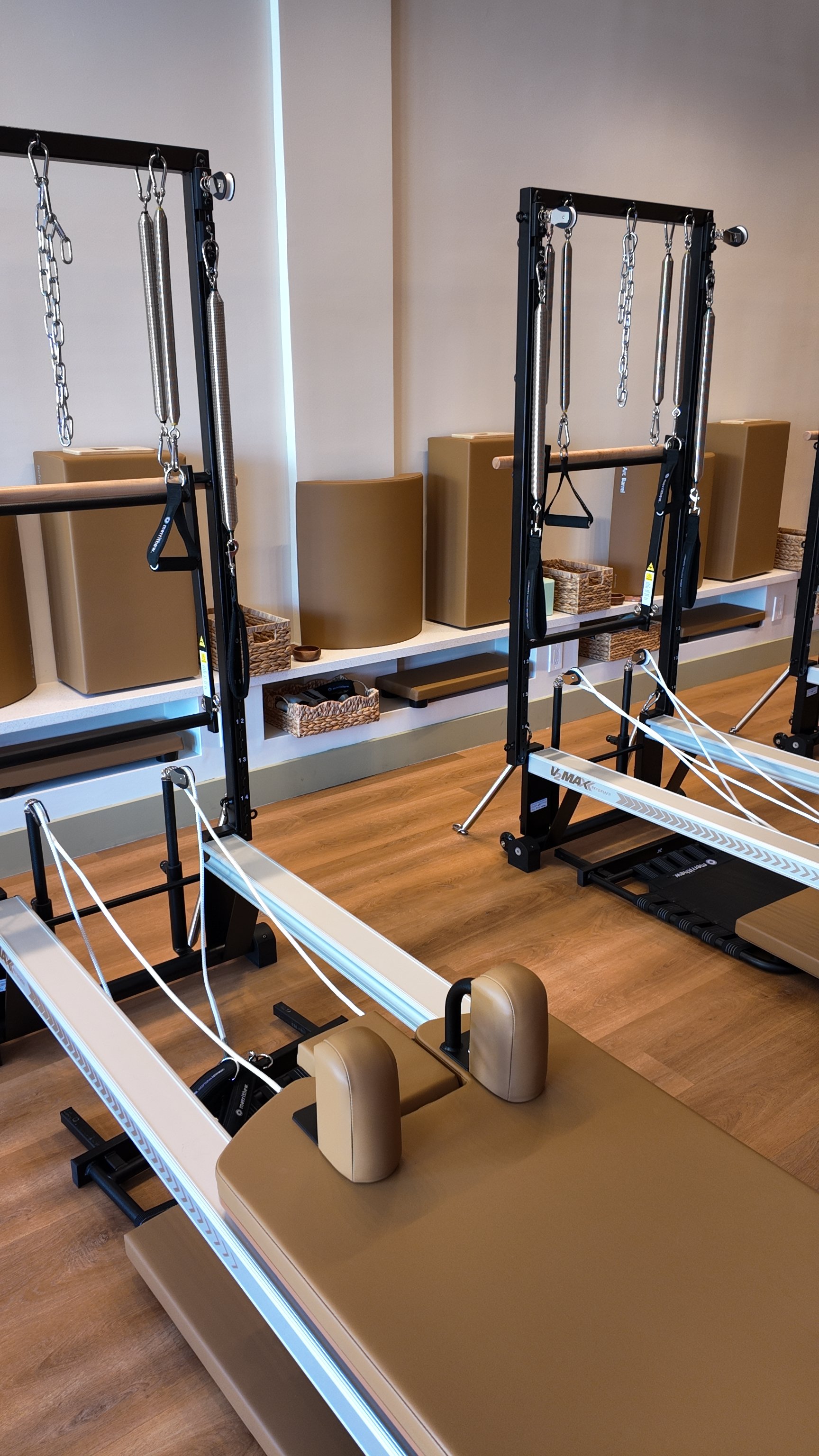 A woman doing a Pilates exercise on a reformer machine in a fitness studio with mirrors and plants.