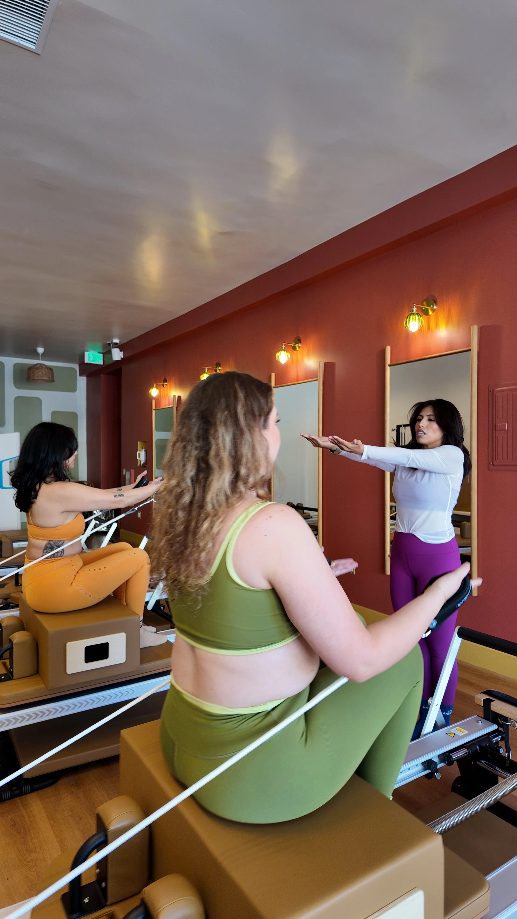 A woman lying on her back on a Pilates reformer machine with her legs elevated in the air and connected to resistance straps.