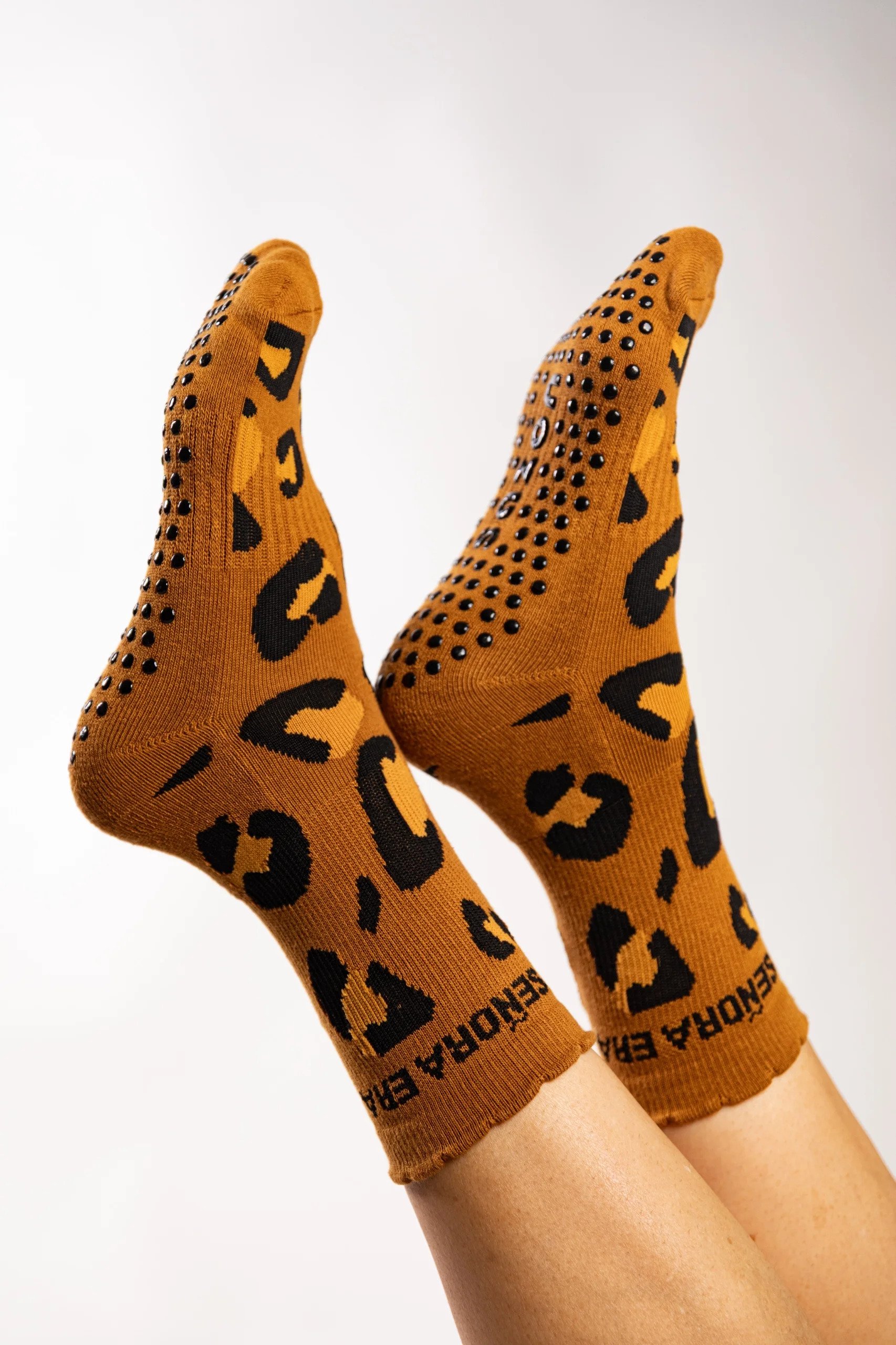 Close-up of two feet wearing orange socks with black animal print and black dots, with the words 'DESENFADORA' and other text visible on the socks, against a plain white background.