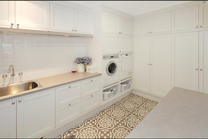 Spacious white laundry with floor to ceiling storage cupboards stainless steel trough overhead cabinetry and decorative patterned floor tiles functional design Melbourne
