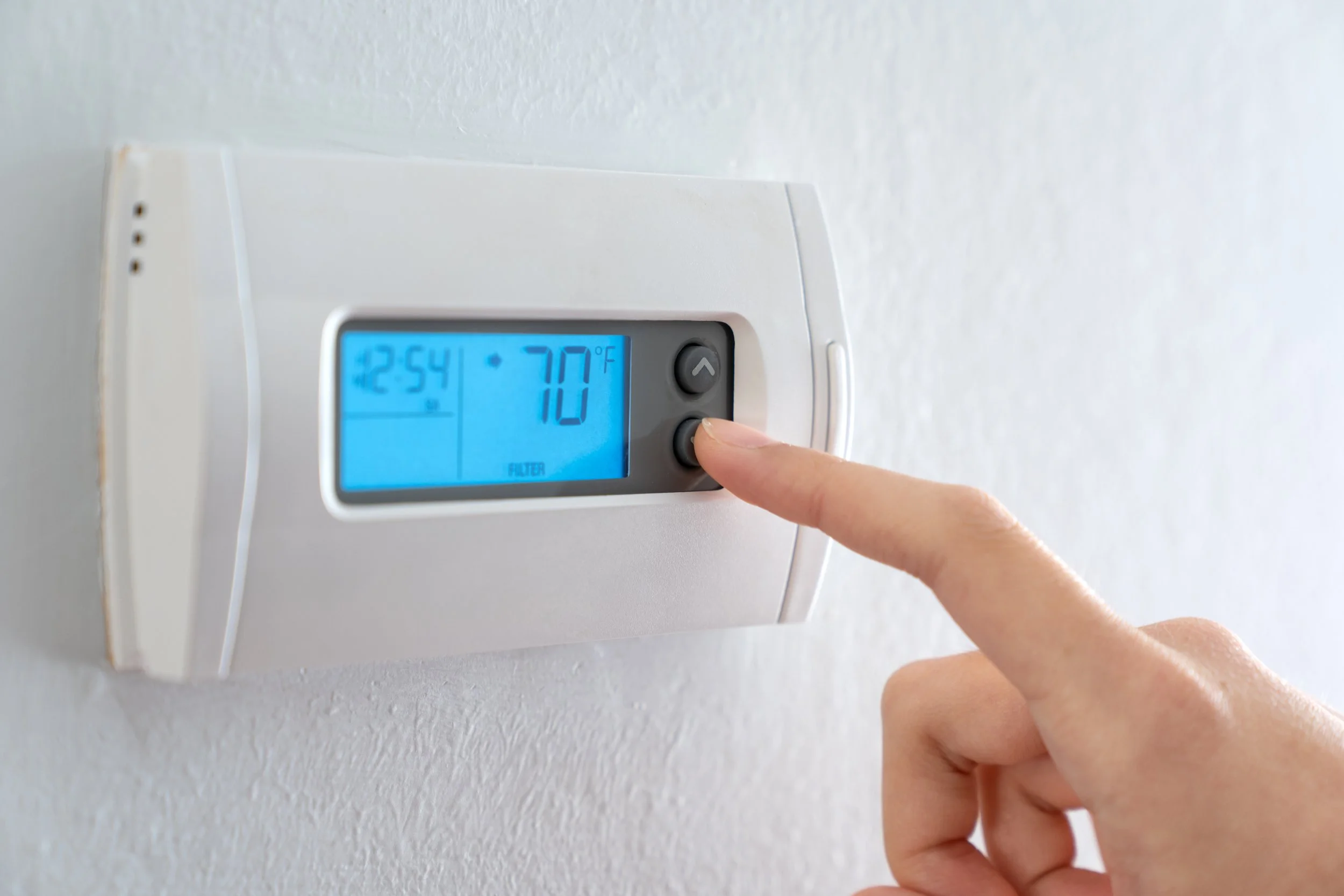 A person's finger adjusting the thermostat on a wall-mounted digital control panel showing 70 degrees Fahrenheit, with the time 12:54 PM displayed on the screen. Thermostat HVAC new replacements repair Lafollette Jacksboro Caryville East Tennessee