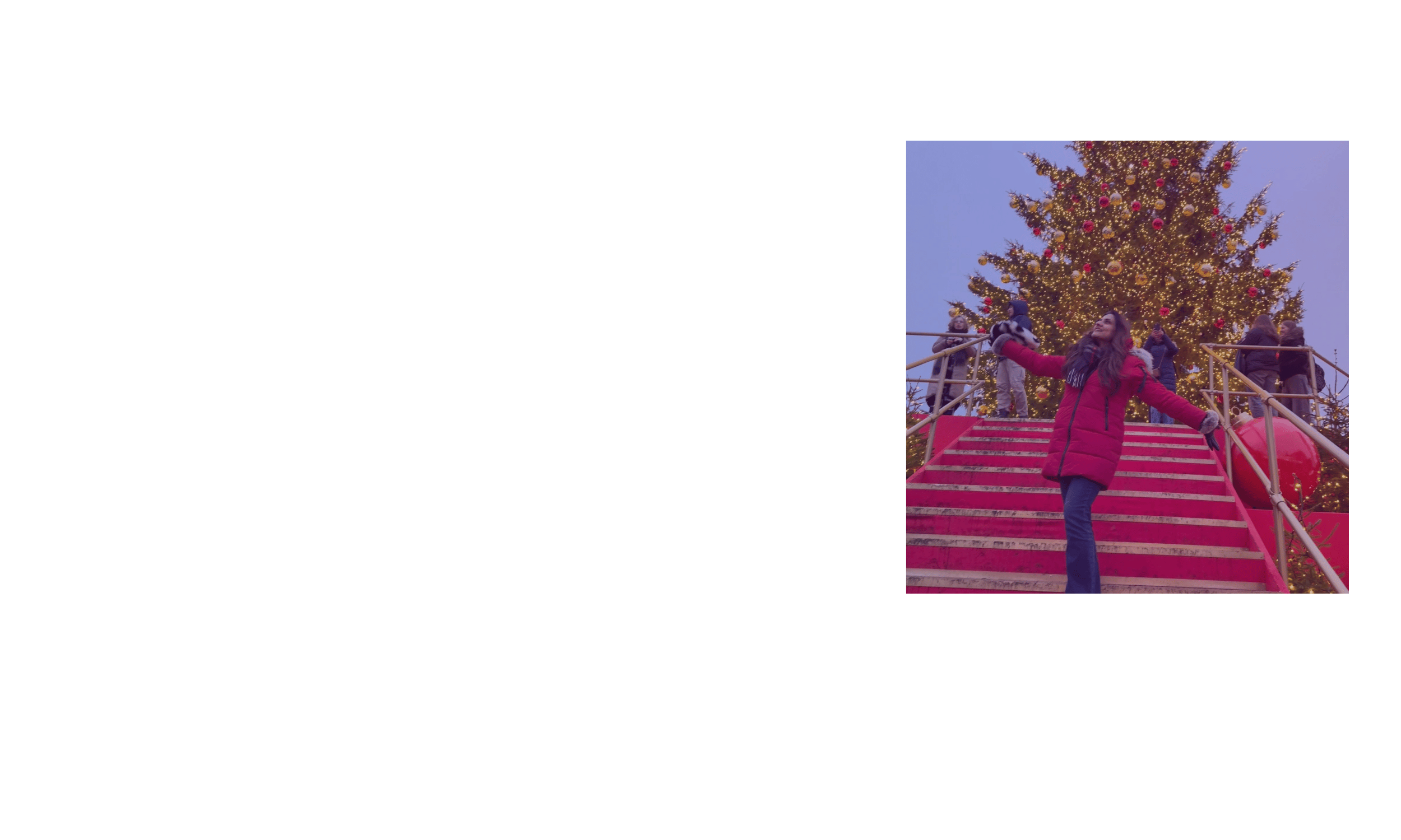 Woman in red winter coat on Christmas decorated stairs outside with a large Christmas tree in the background and people around.
