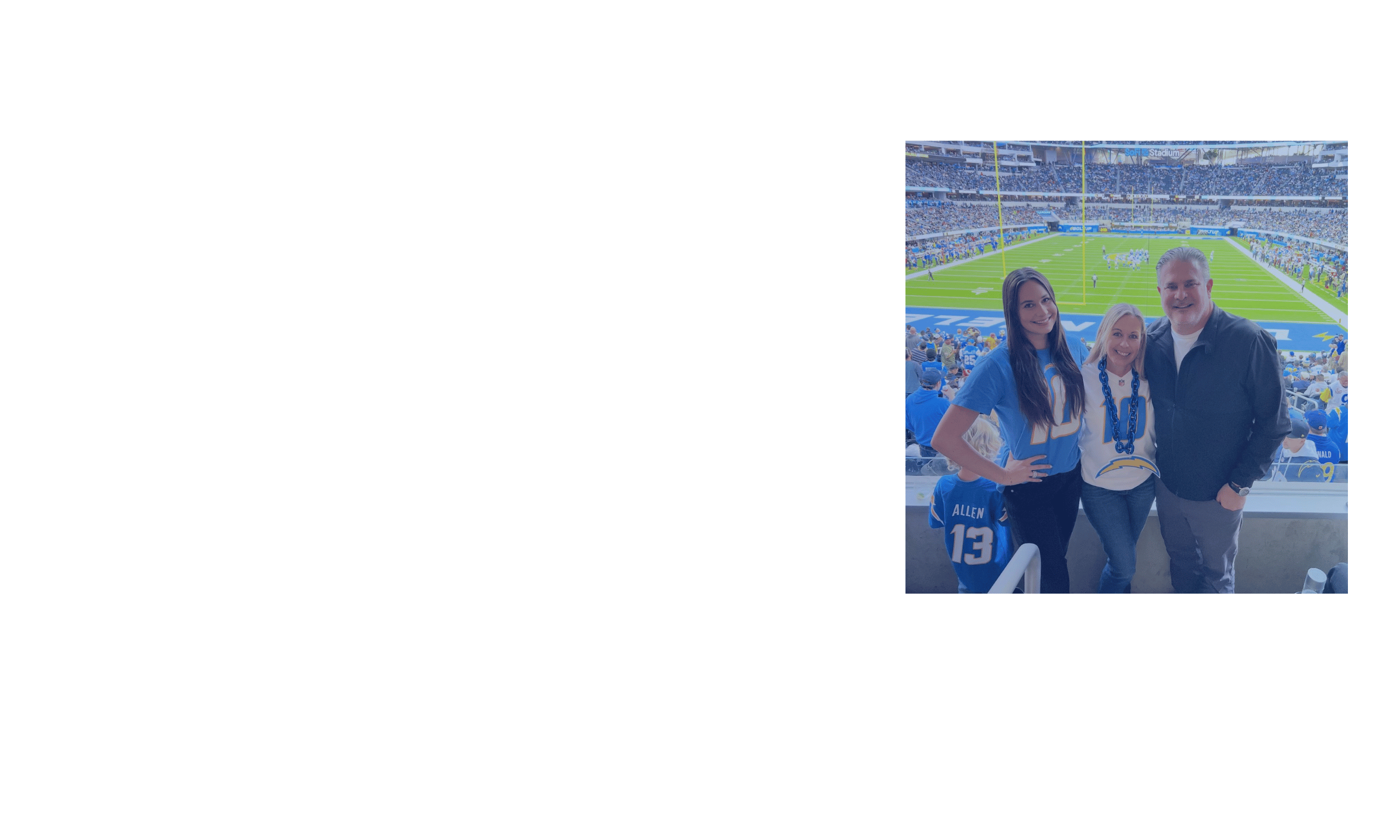 Three people at a football game in a stadium, smiling at the camera, with a field and audience in the background.
