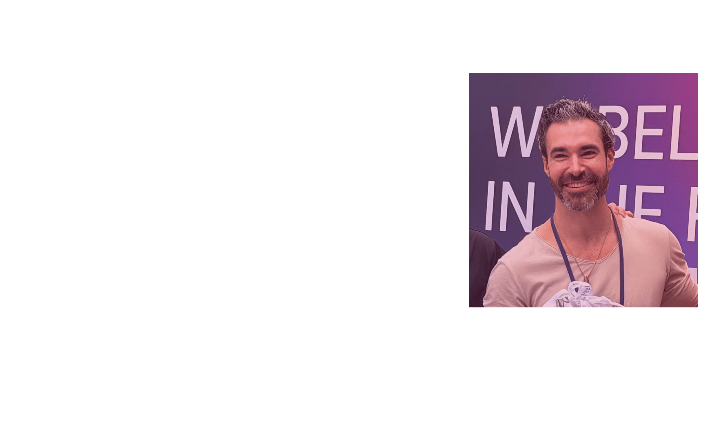 Smiling man with dark hair and beard at an event with a sign in the background that says 'WOBEL IN THE'.
