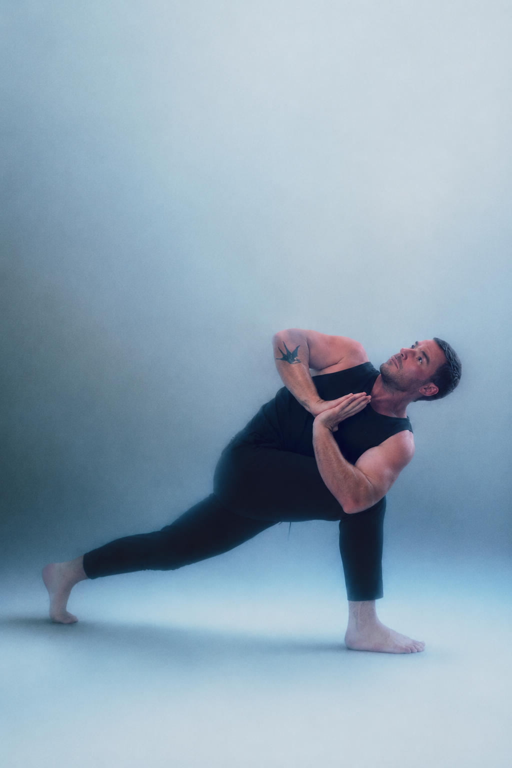 Chris Magee practicing yoga in a strong position with hands in prayer.