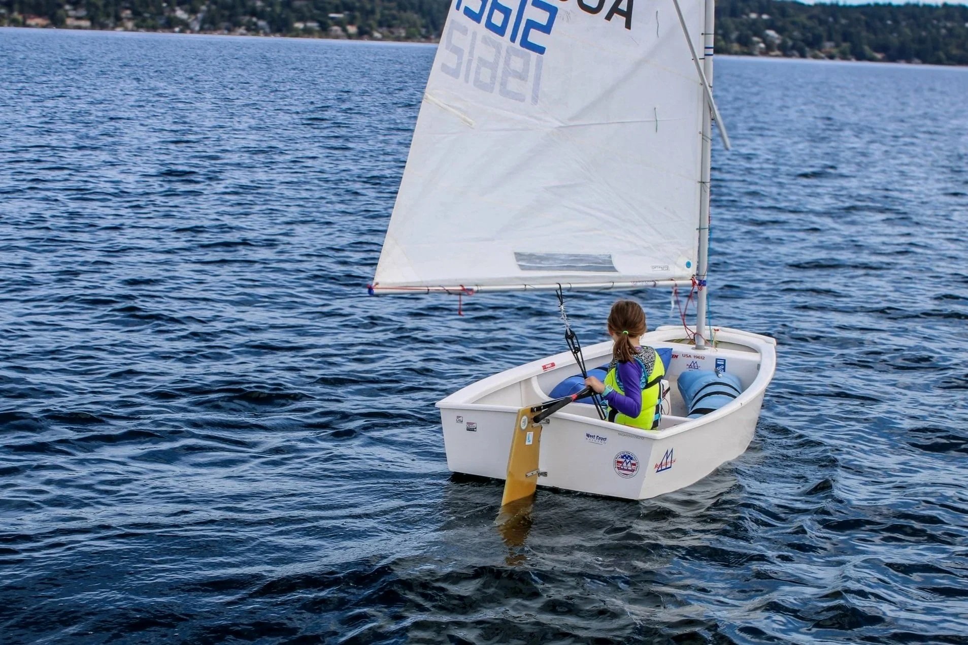 A girl sailing a small white boat with a sail on a body of water.