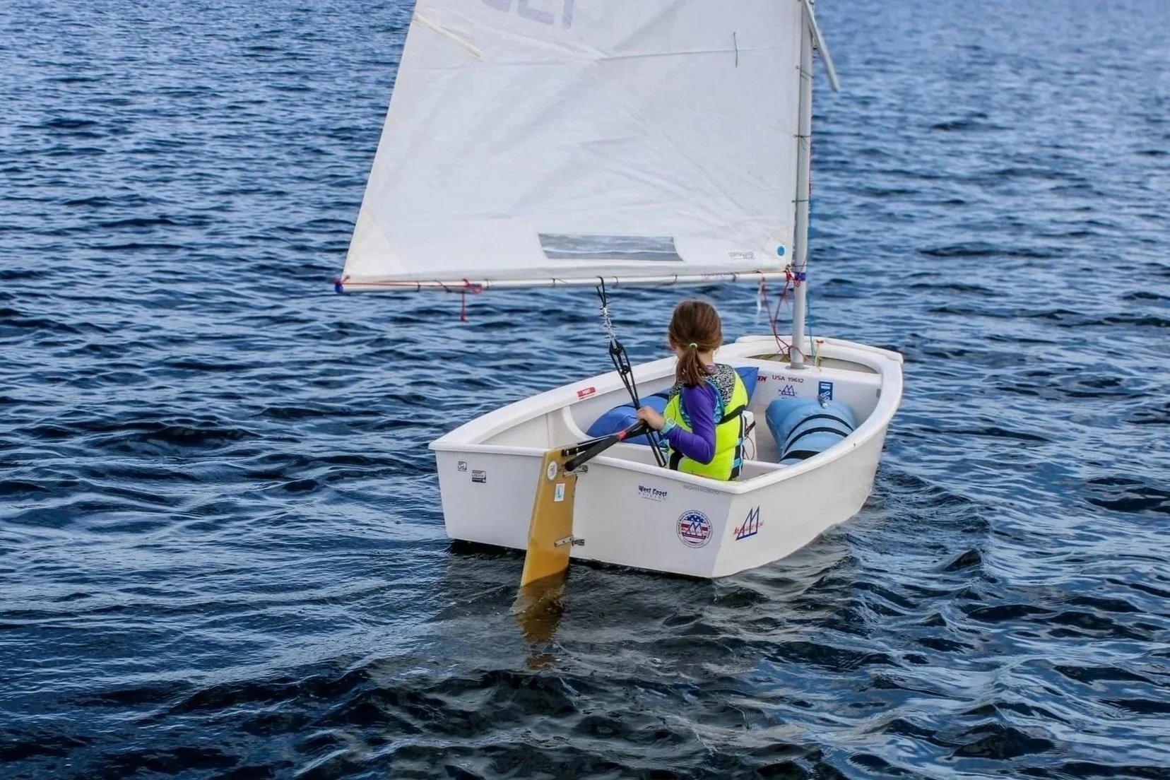 A girl sailing a small white boat with a sail on a body of water.