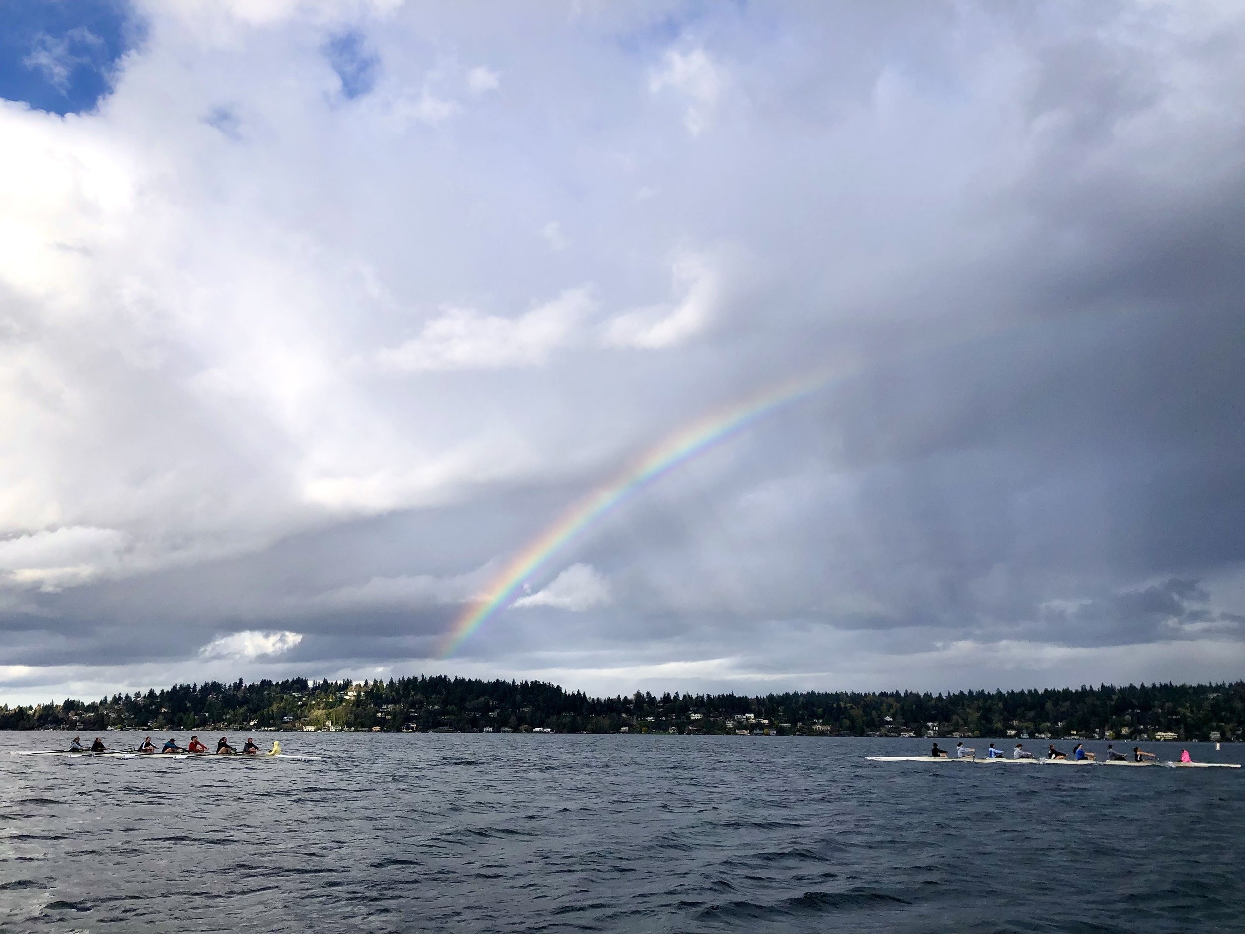 a rowing picture with 2 eight person boats and a rainbow.