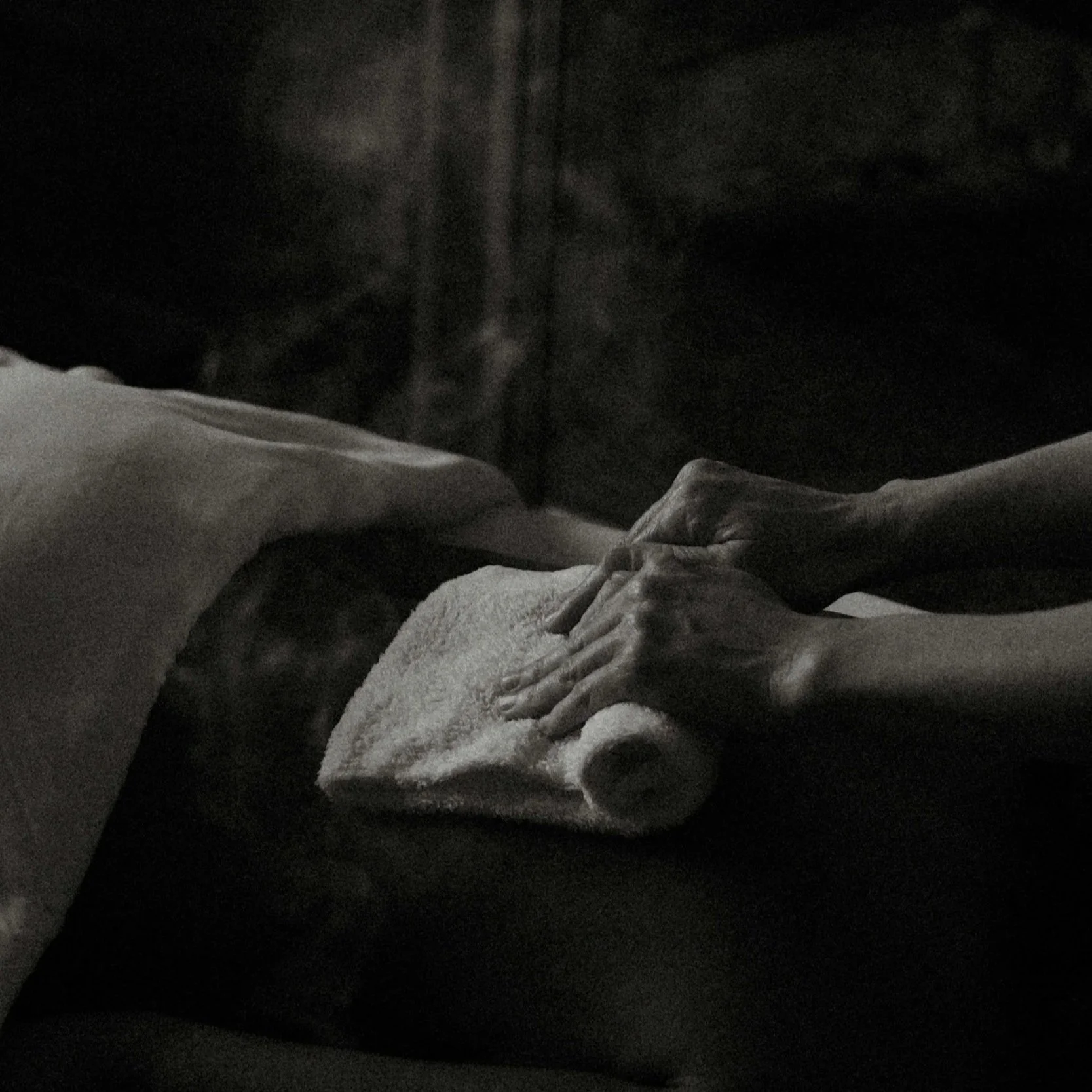 A person receiving a hot towel therapeutic massage treatment, with only their head and back visible, while a massage therapist moves the hot towel.