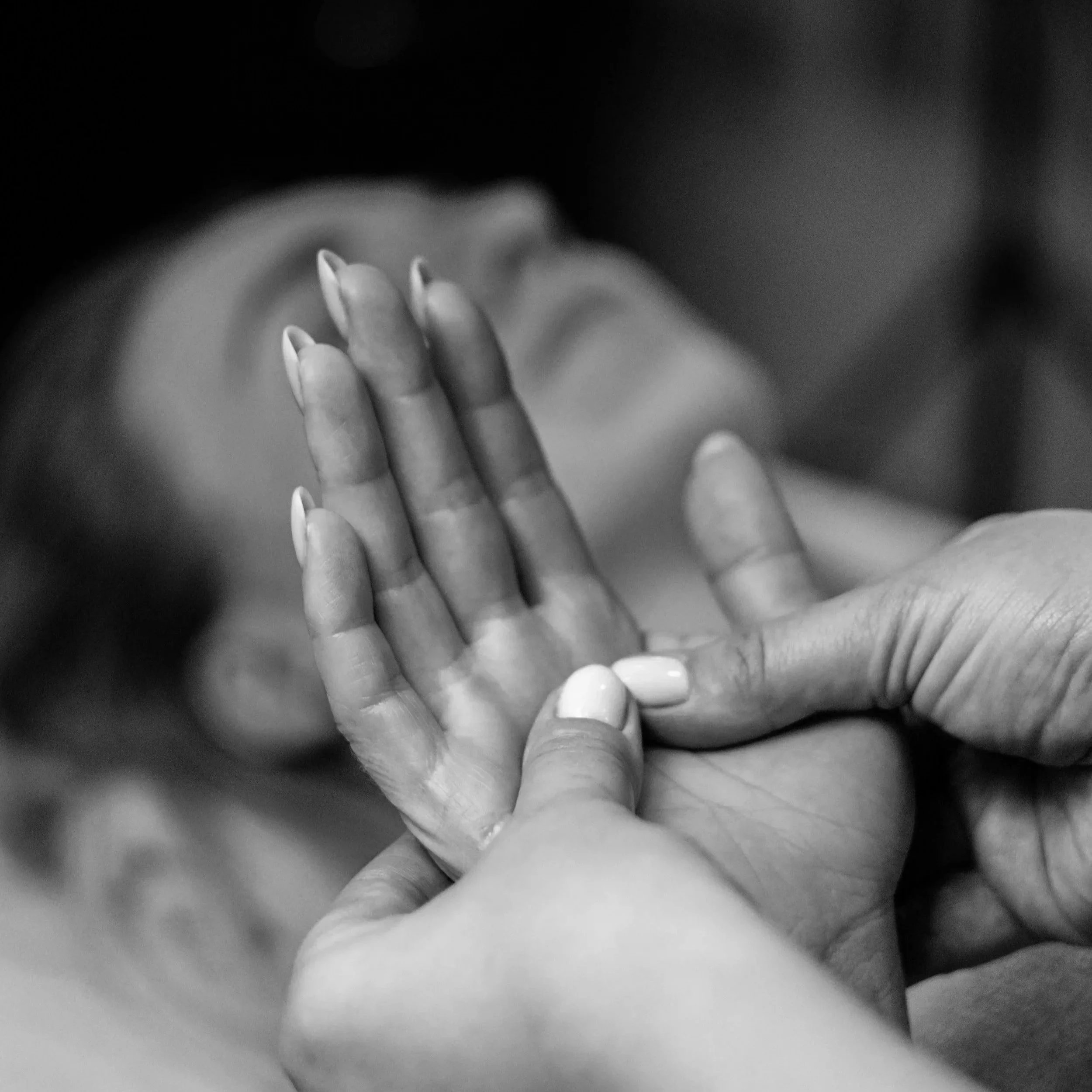 Close-up of a person's hand with manicured nails receiving a hand massage, seen in black and white.