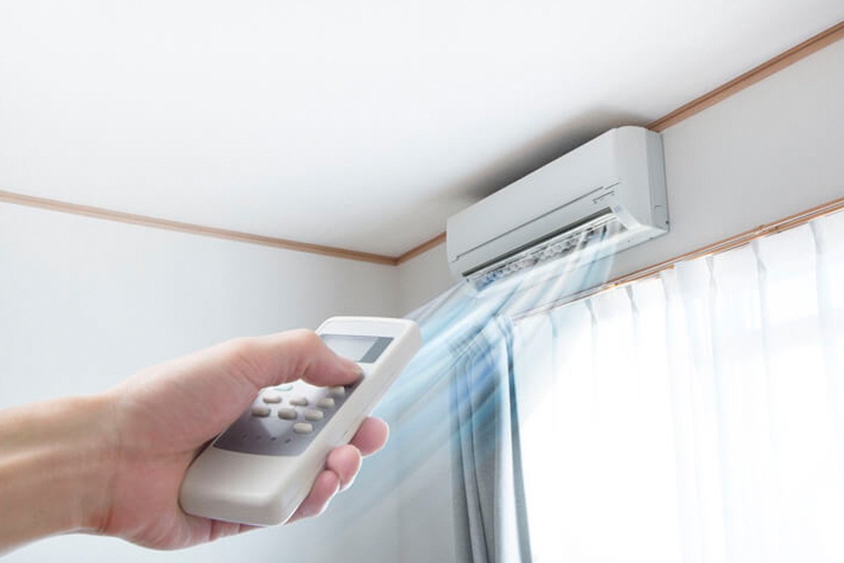 A person using a remote control to turn on an air conditioner in a room with white curtains.