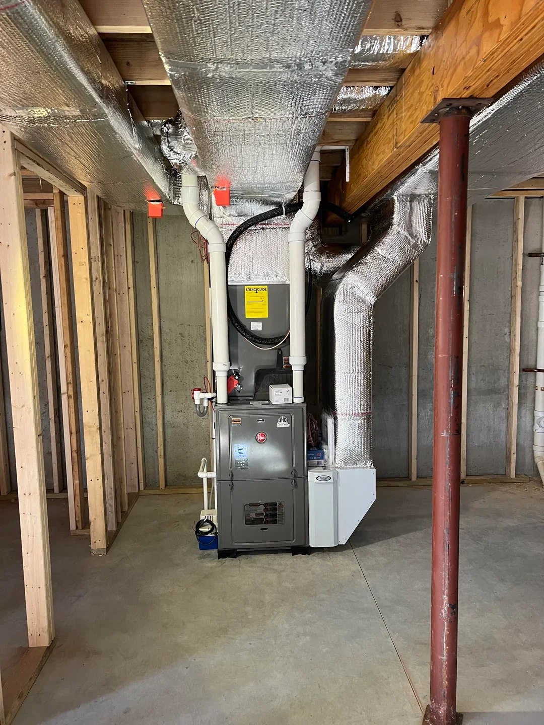 View of a furnace and ventilation system in an unfinished basement with wooden framing and concrete floor.