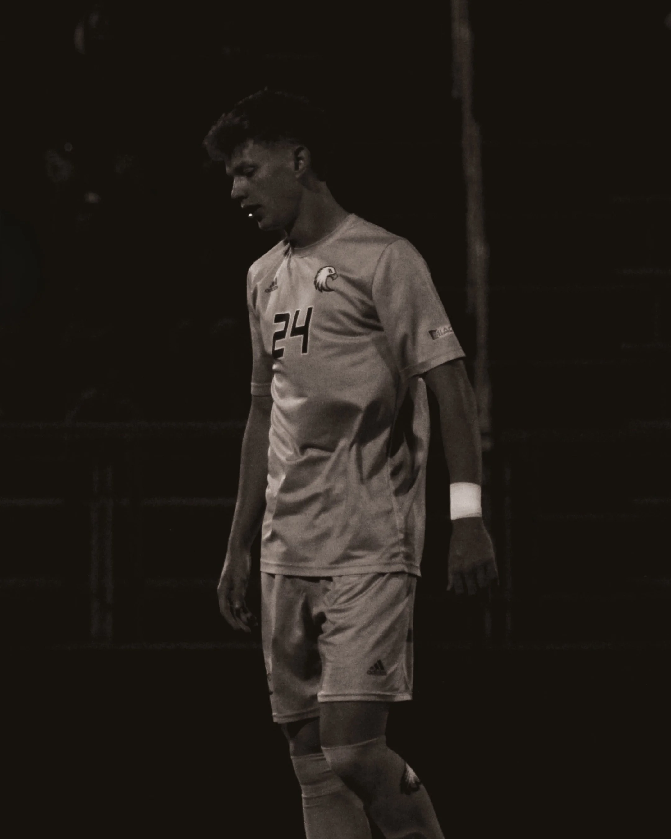 A young male soccer player standing on the field at night, wearing a sports uniform with the number 24 and a logo on his shirt and shorts.