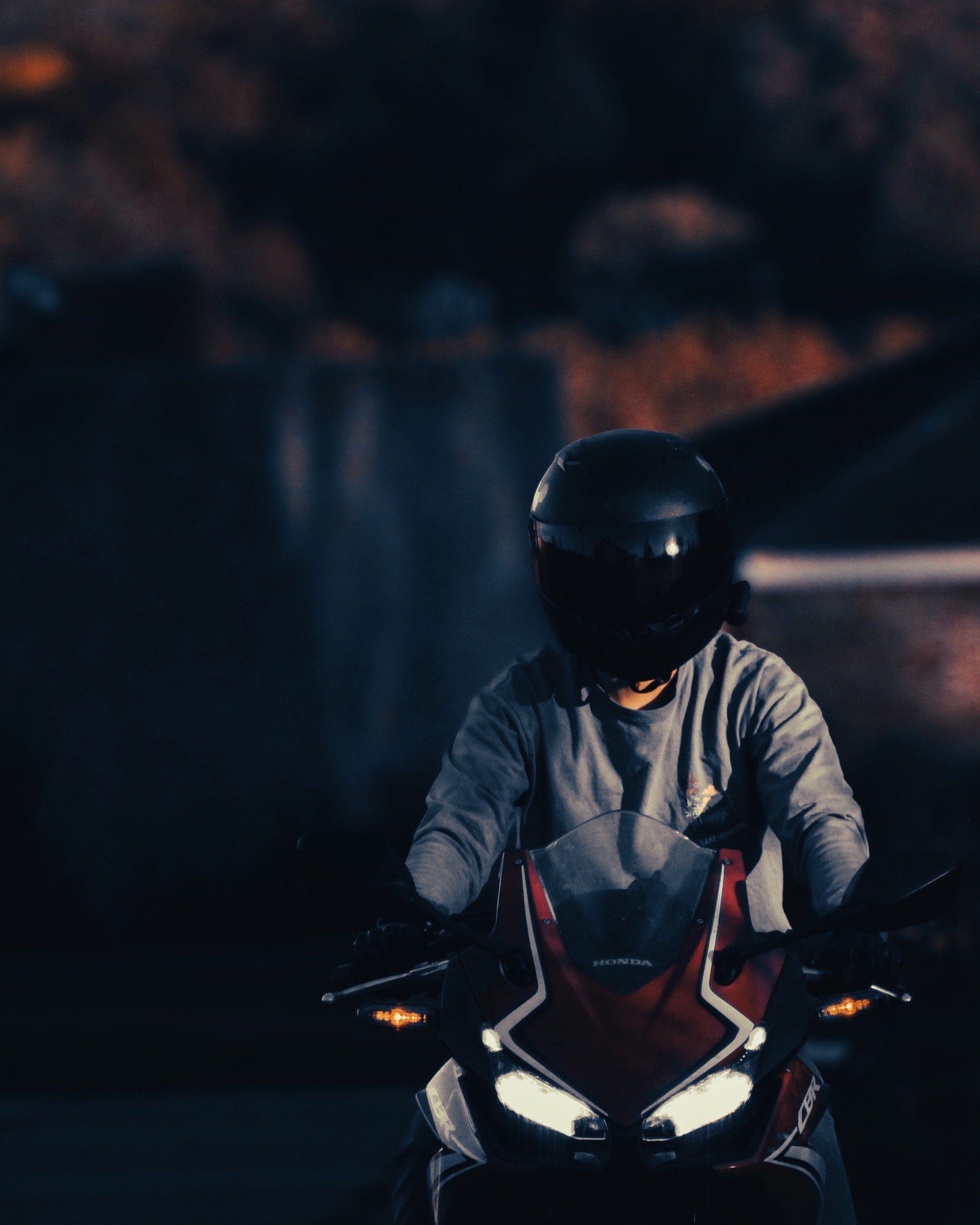 A photograph captured by Aleka London of a person wearing a helmet riding a motorcycle at dusk, with a dark background and illuminated headlights.