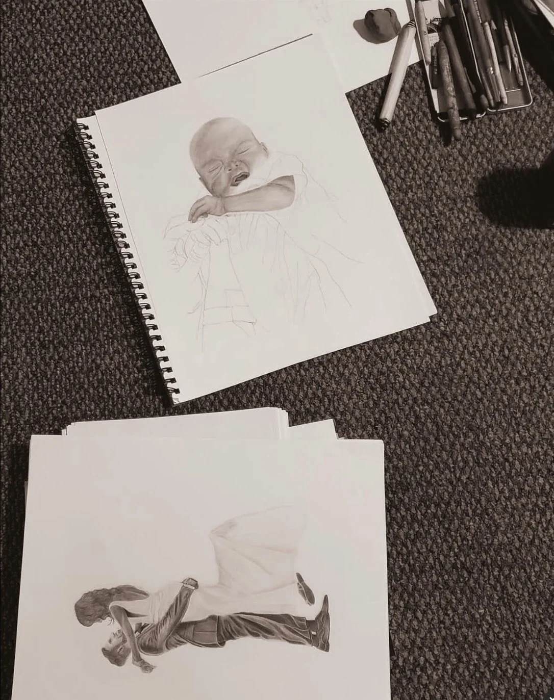 Two sketches on paper, one of an infant and one of a wedding photo of a man lifting his wife up in her long beautiful dress.