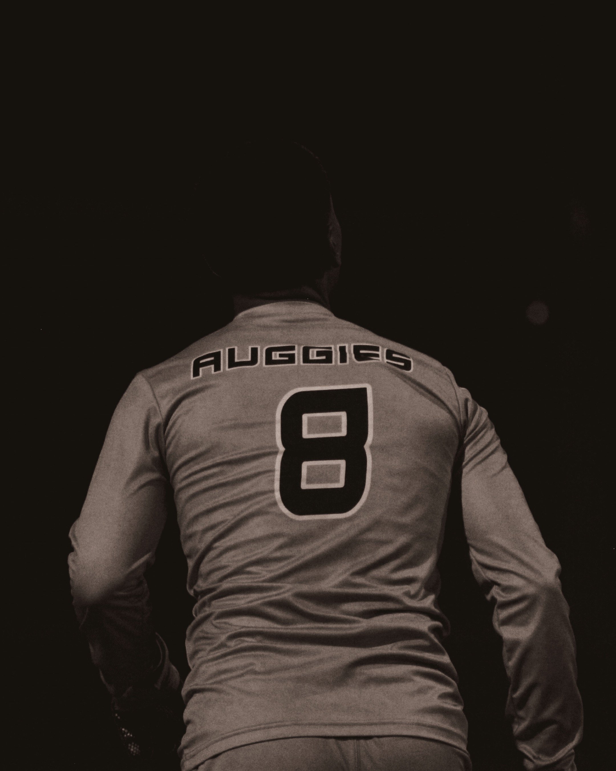 Back view of a basketball player wearing a jersey with the name 'AUGGIES' and the number 8, standing in a dark setting.