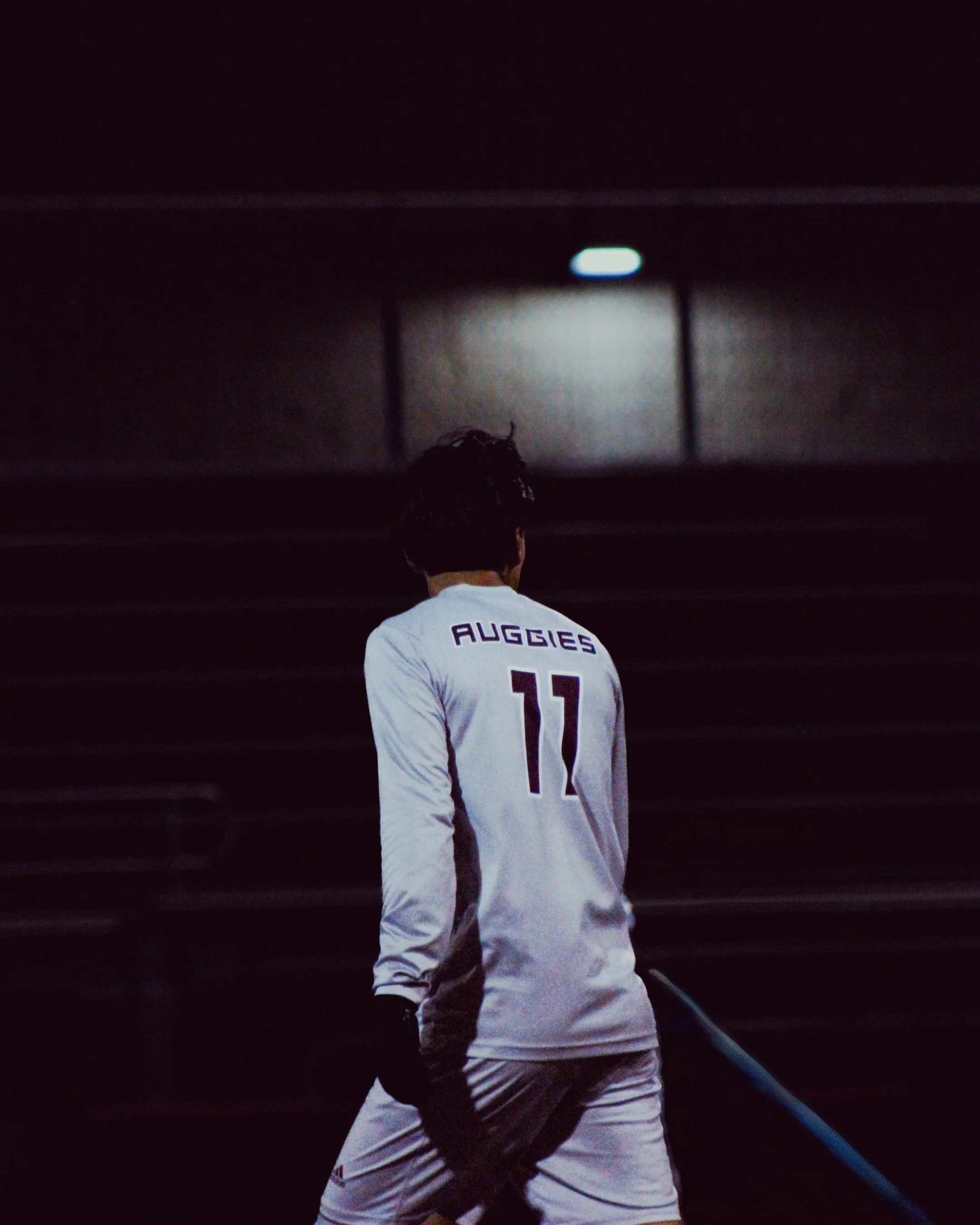 A person wearing a white sports jersey with the name 'Auggies' and the number 11 on the back, holding a hockey stick