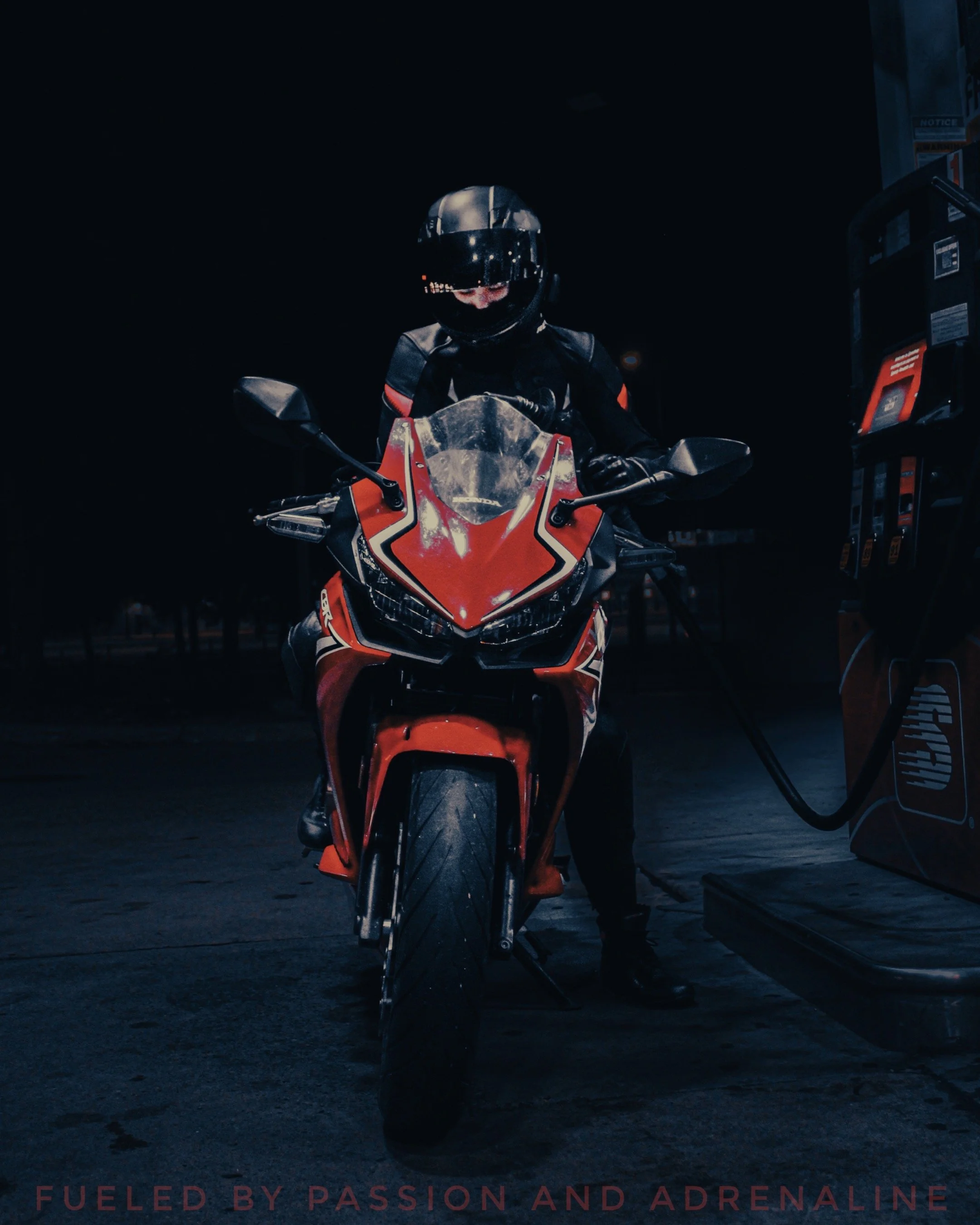 A motorcyclist in black gear and helmet filling a red sports motorcycle with fuel at a gas station during nighttime.