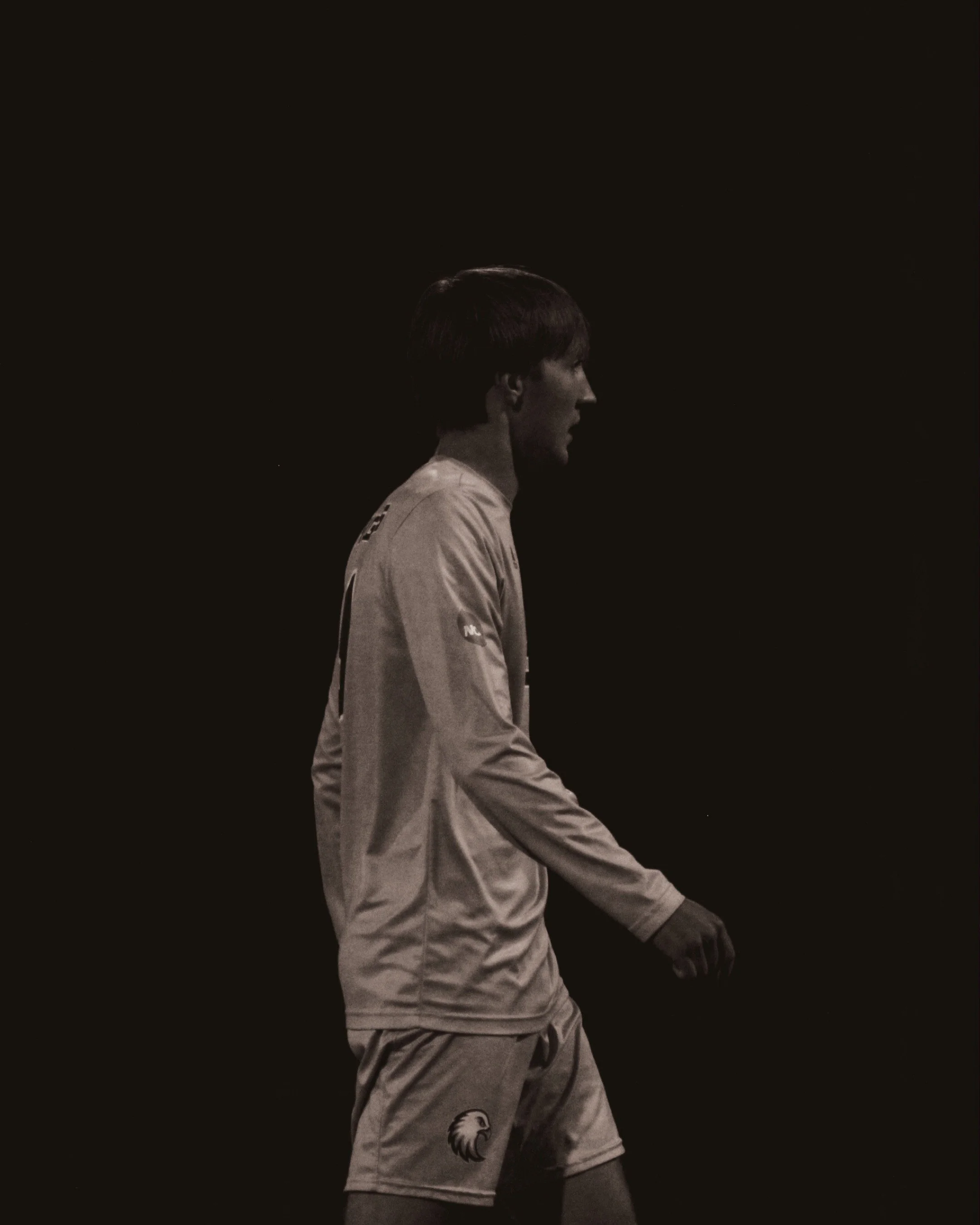 A young male athlete in a sports uniform walking against a dark background.