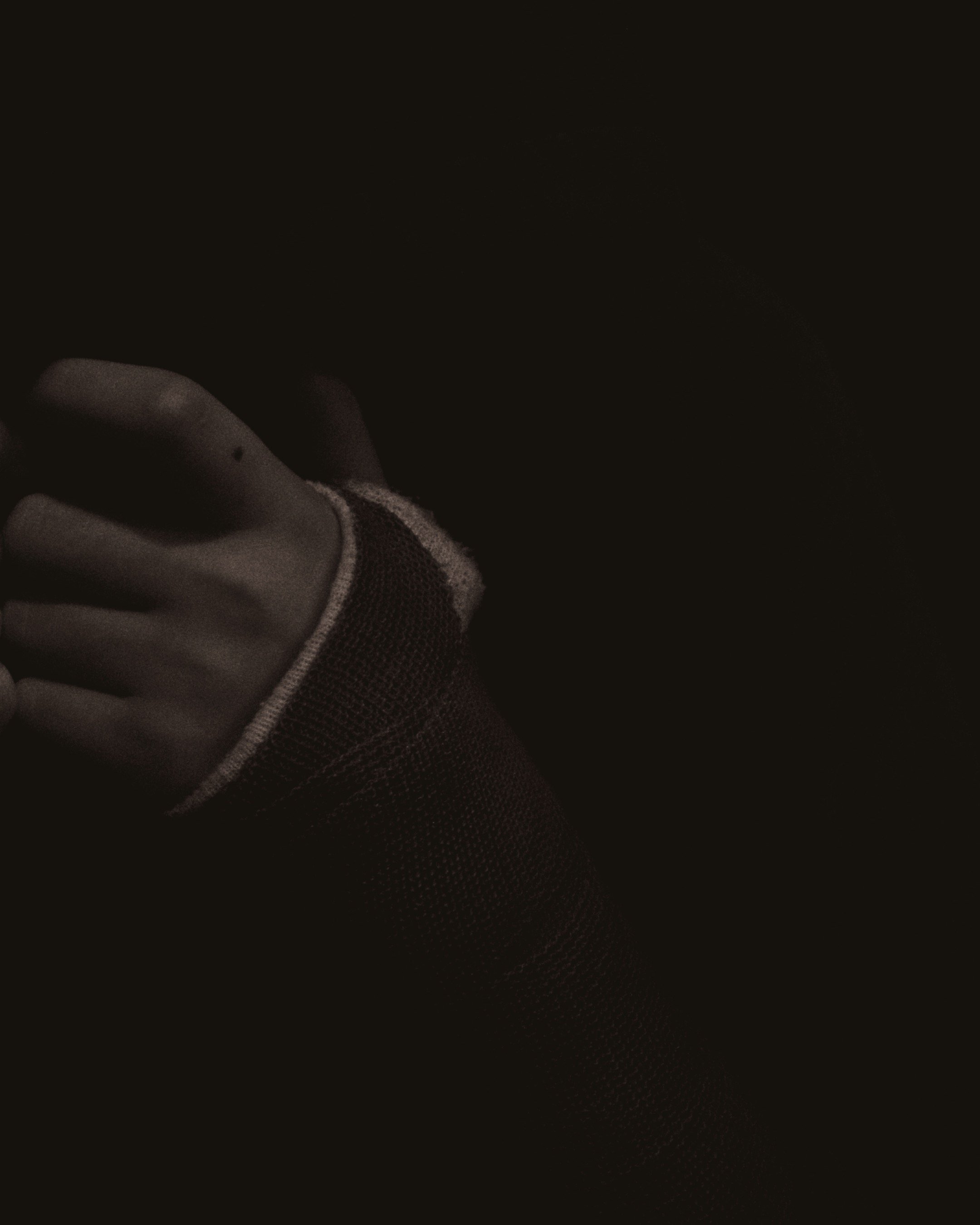 Close-up of a hand in a black glove, with the thumb wrapped in a mesh or sports glove fabric, set against a dark background.