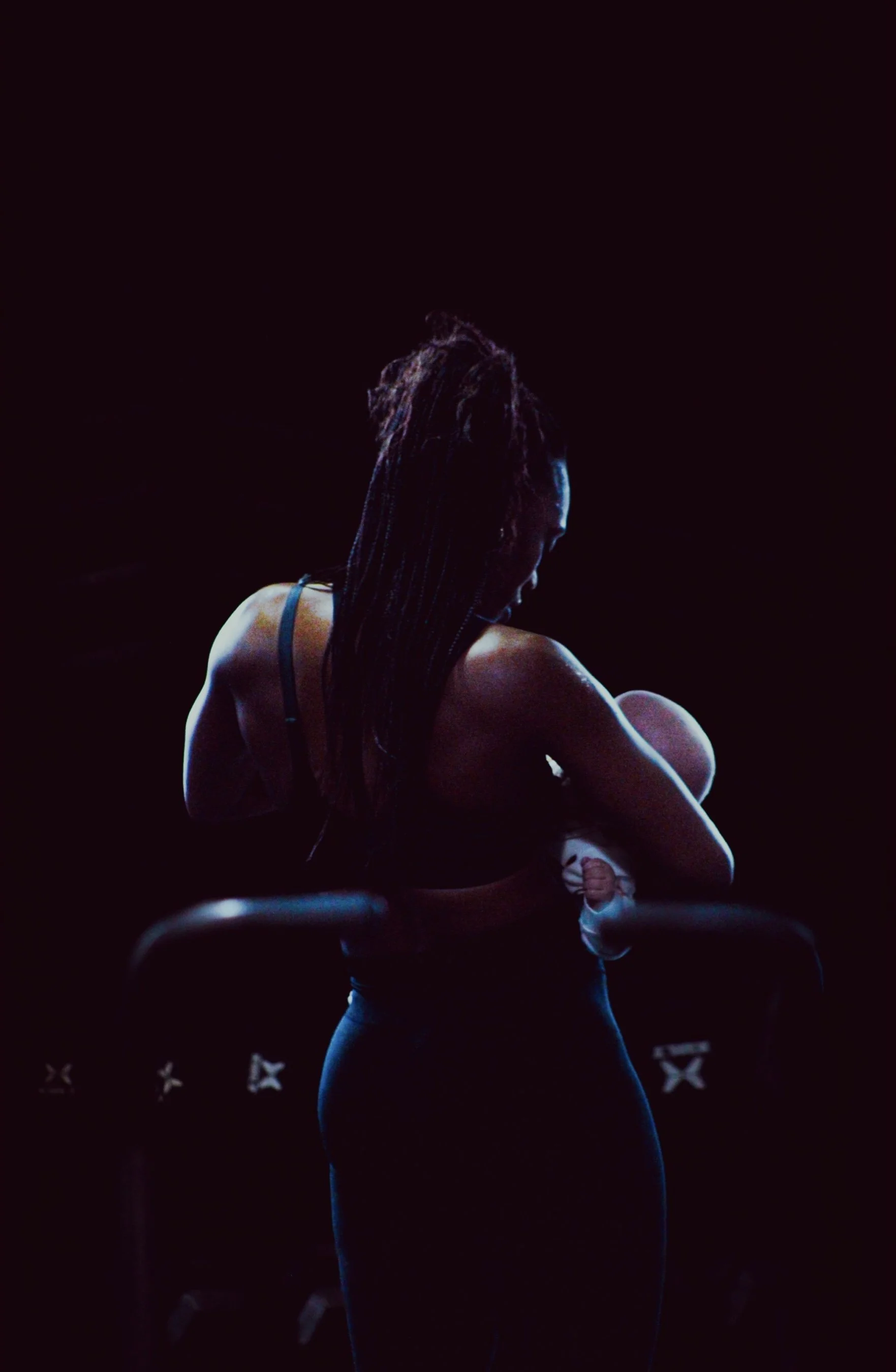 A woman with dreadlocks sitting on a chair, cradling a baby in her arms in a dark setting with minimal lighting.