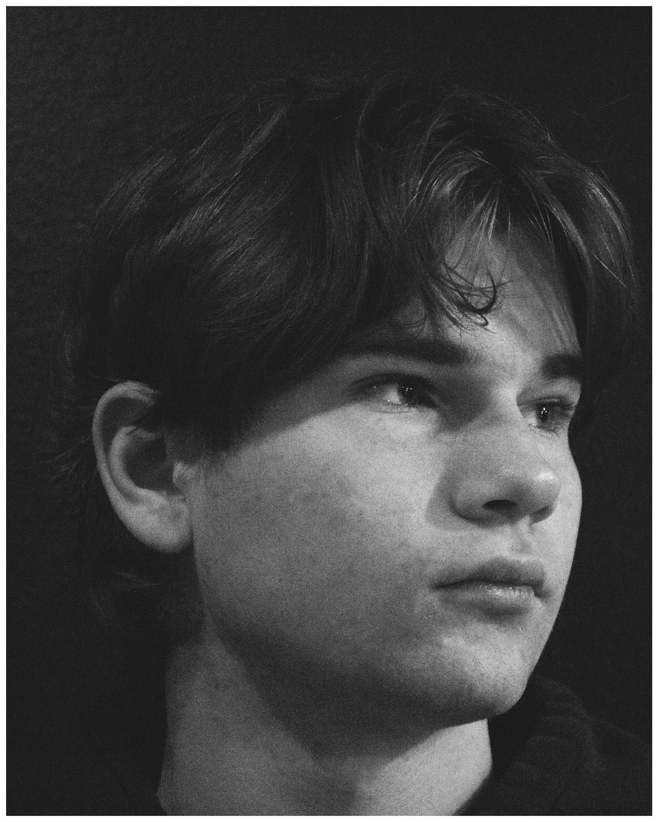 Black and white close-up portrait of a young man with wavy hair, looking to the side.