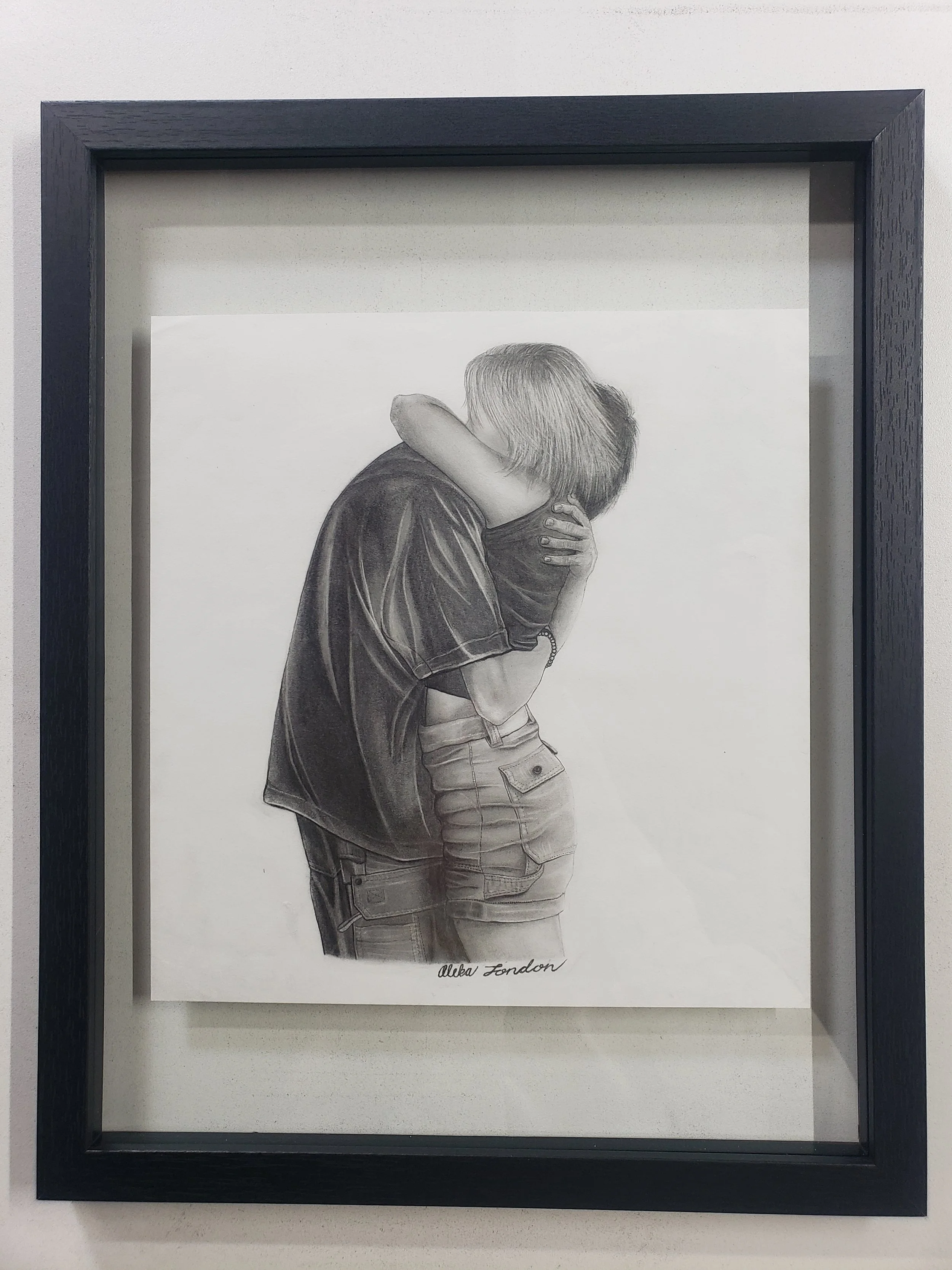 A detailed black and white pencil drawing of two adults newly engaged embracing. Signed by Aleka London at the bottom.