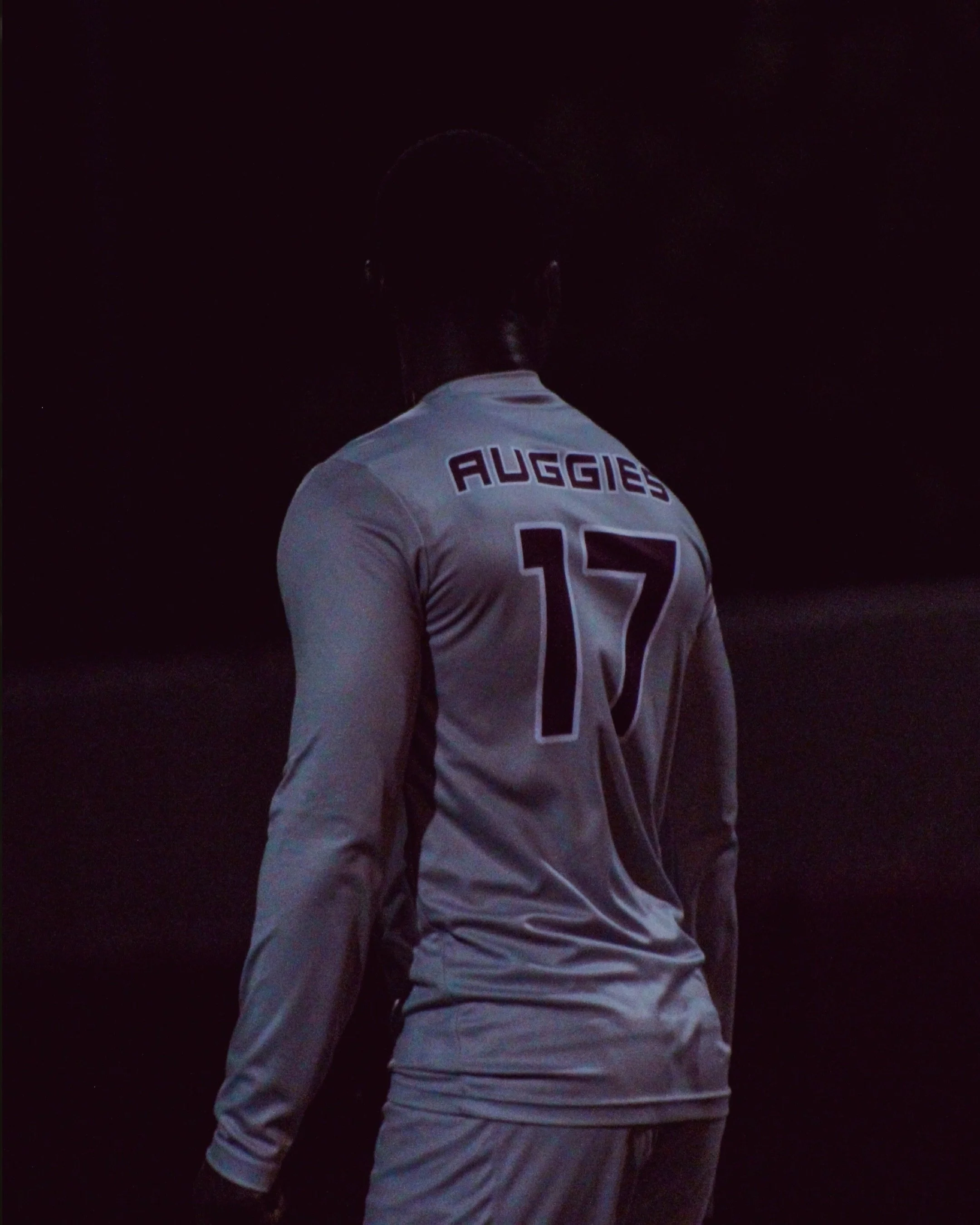 Back of a soccer player in a jersey with 'Auggies' and the number 17, standing in a dark environment.