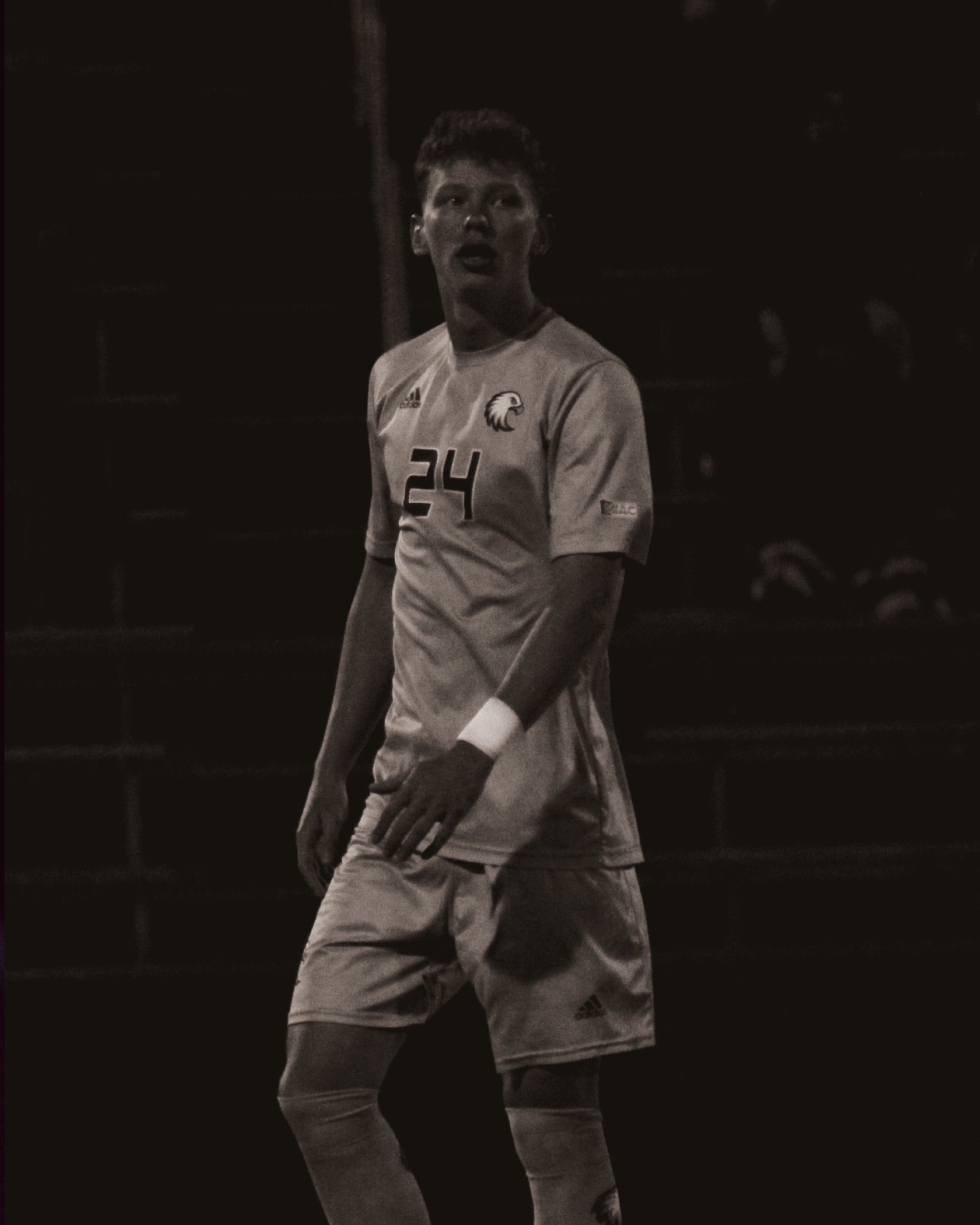 A young male soccer player standing on the field during a game, wearing a sports uniform with the number 24 and an eagle logo.