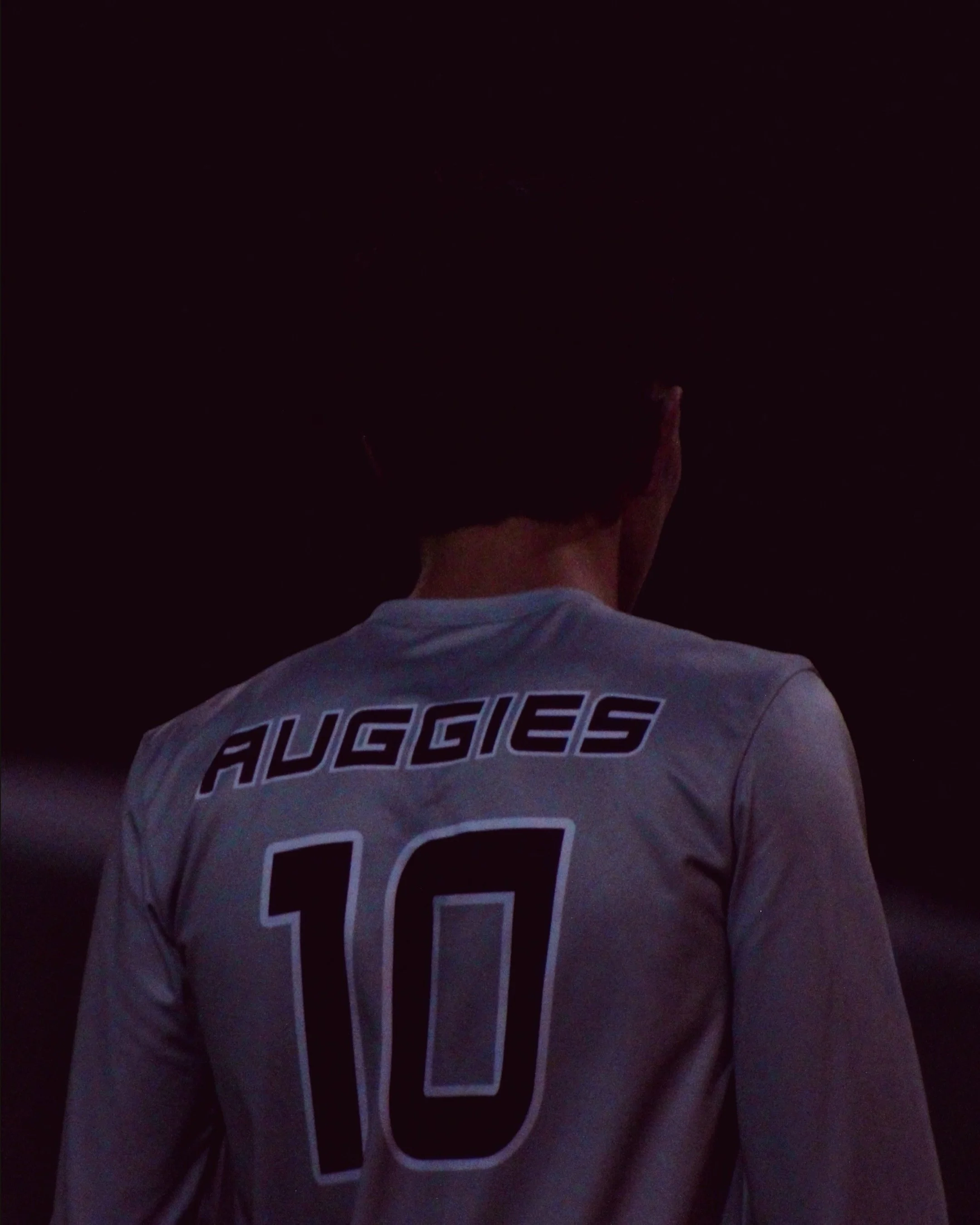 Back of a football player wearing a jersey with the name 'AUGGIES' and the number 10, dark background.