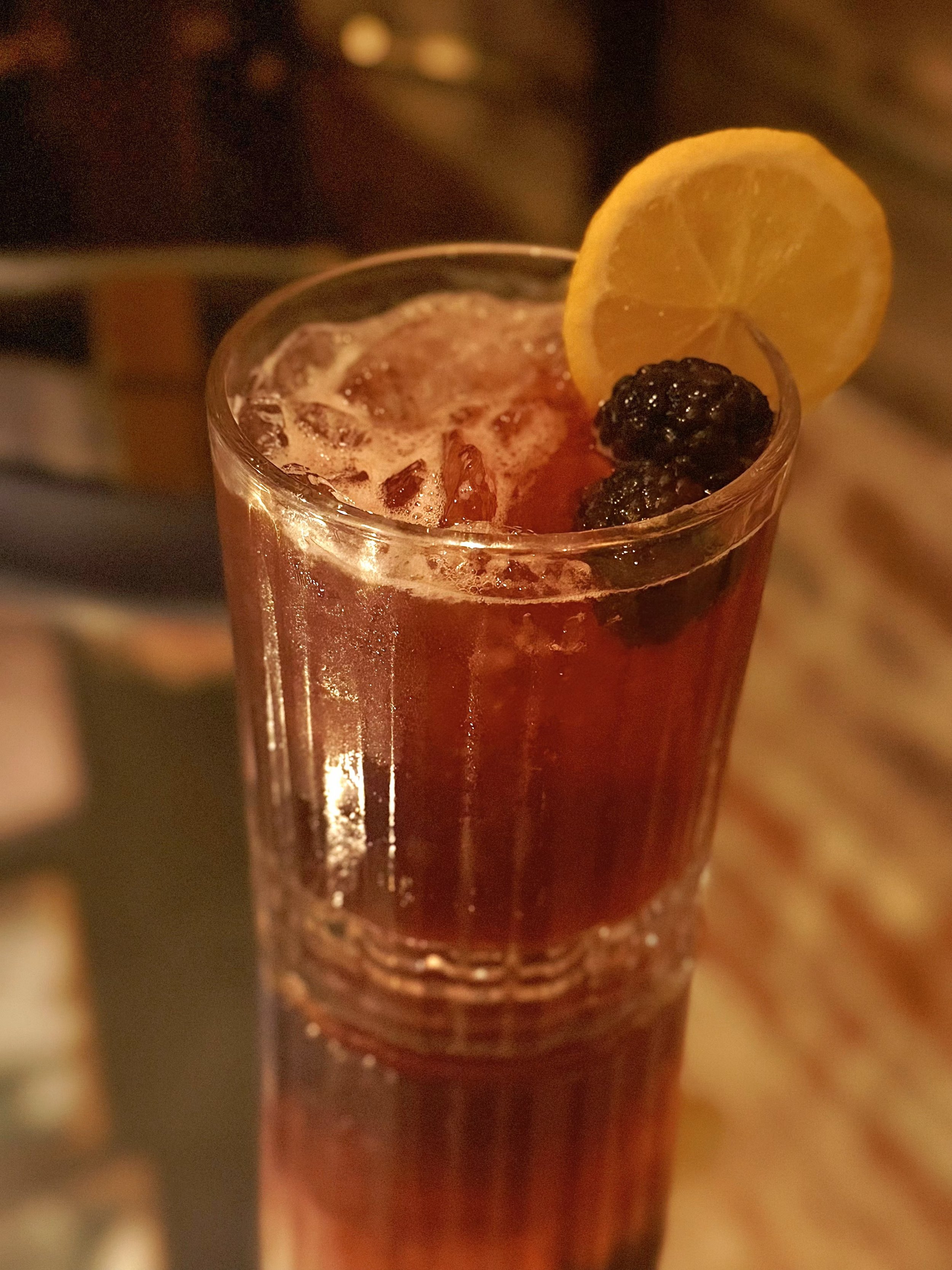 A tall glass of iced tea garnished with a lemon wedge and blackberries.