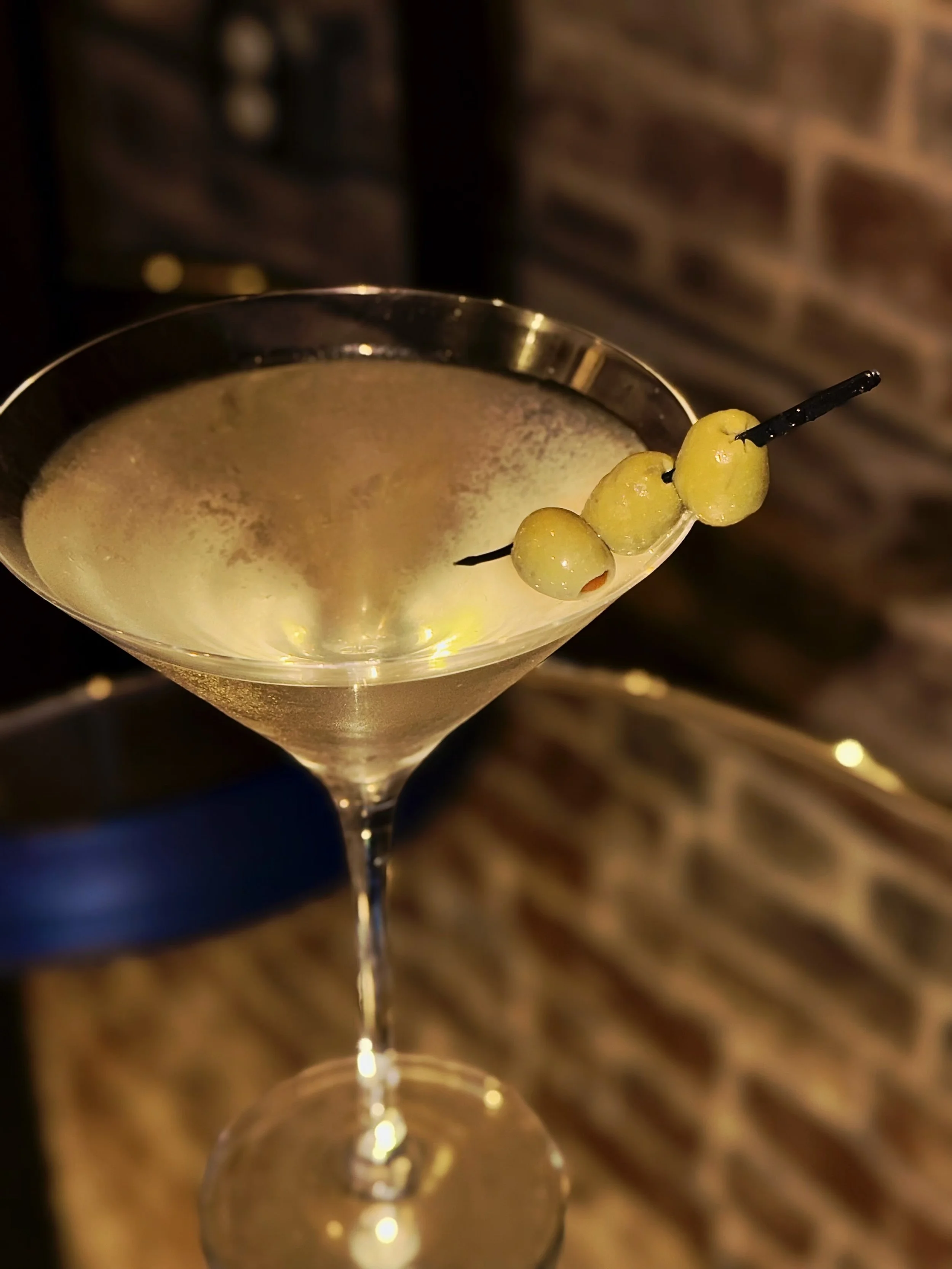 A cocktail in a martini glass garnished with three green olives on a skewer.