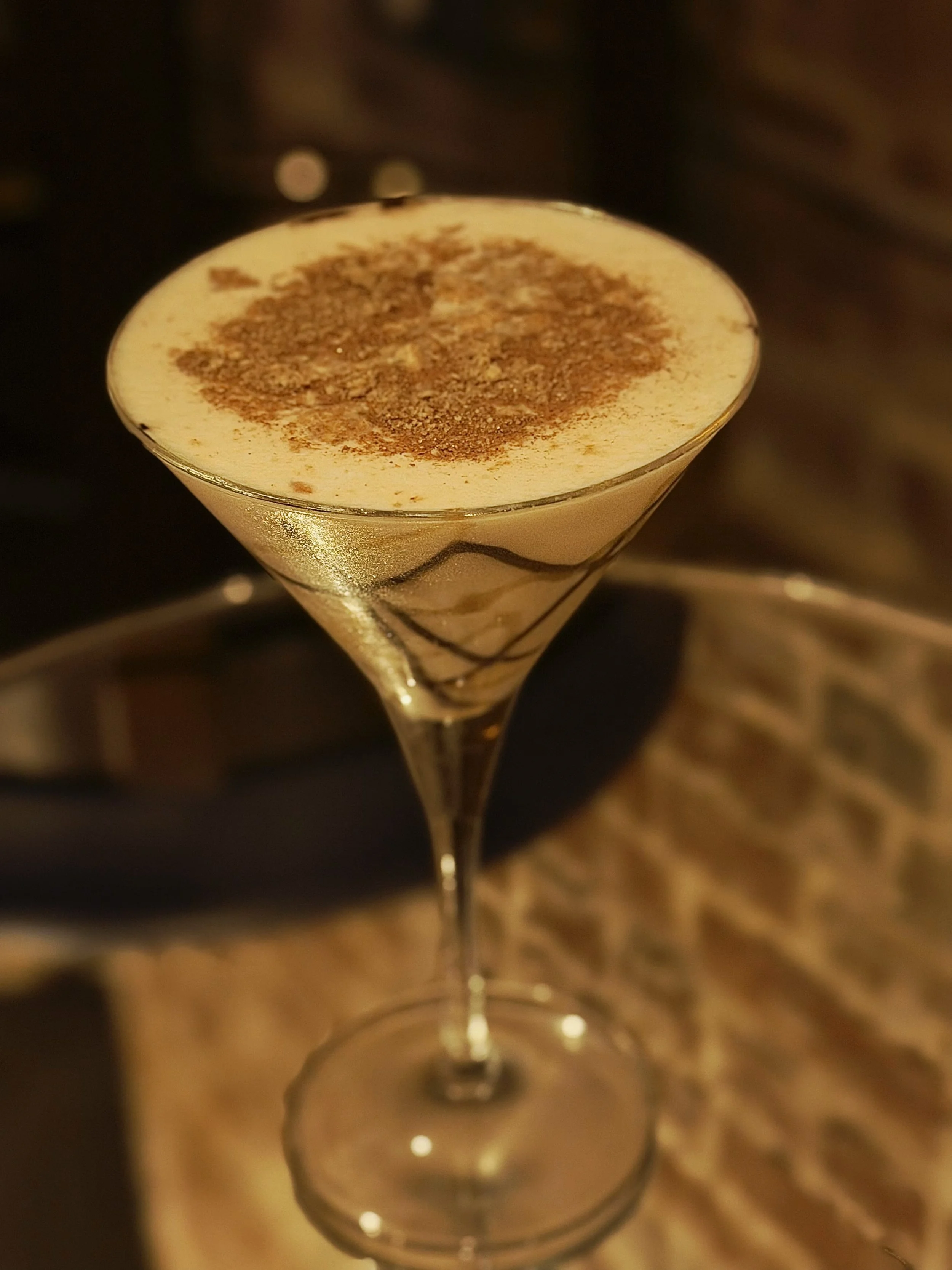 A cocktail in a martini glass topped with whipped cream and sprinkled with cocoa powder.