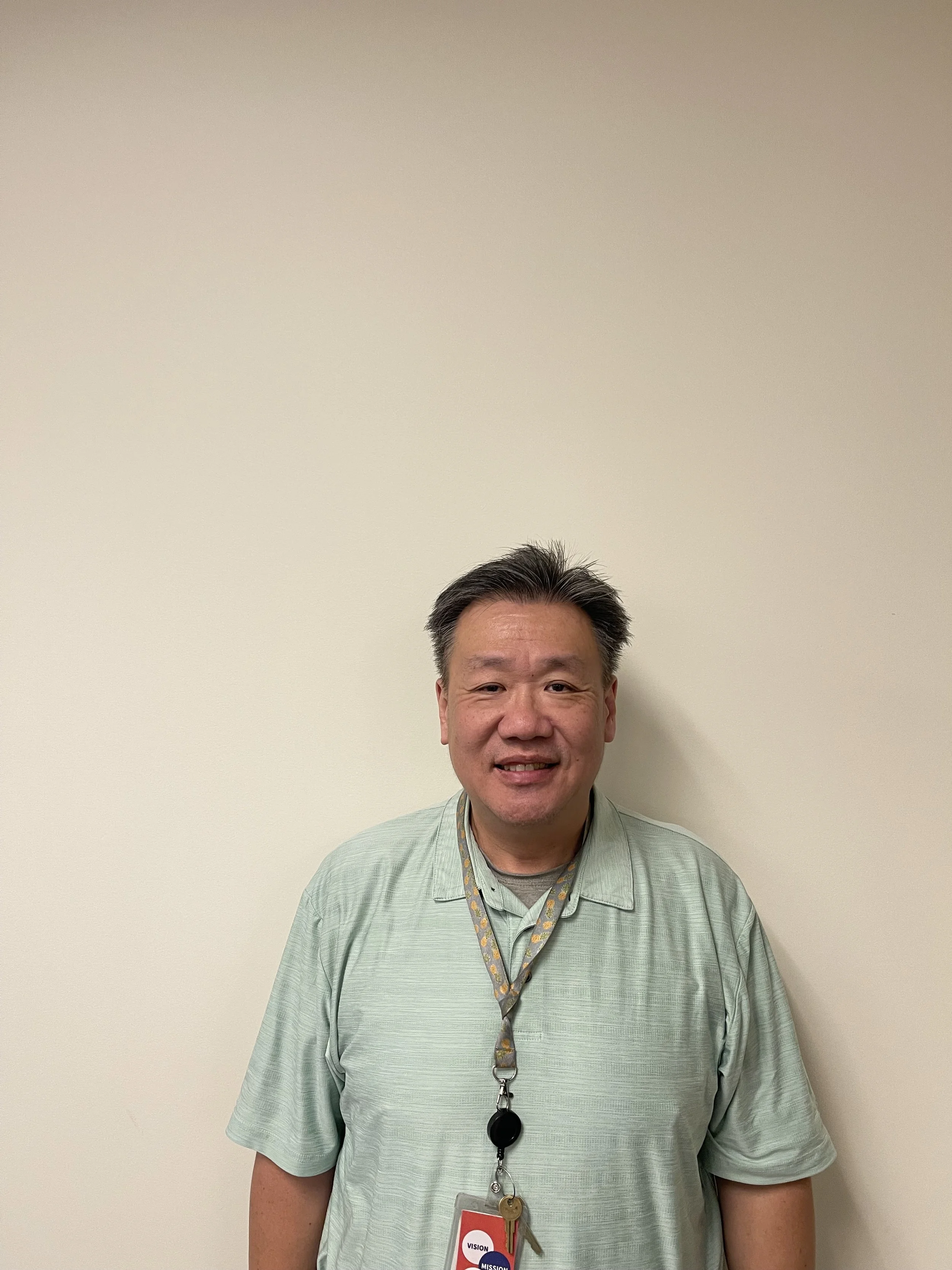 Man in green polo standing against a white wall smiling