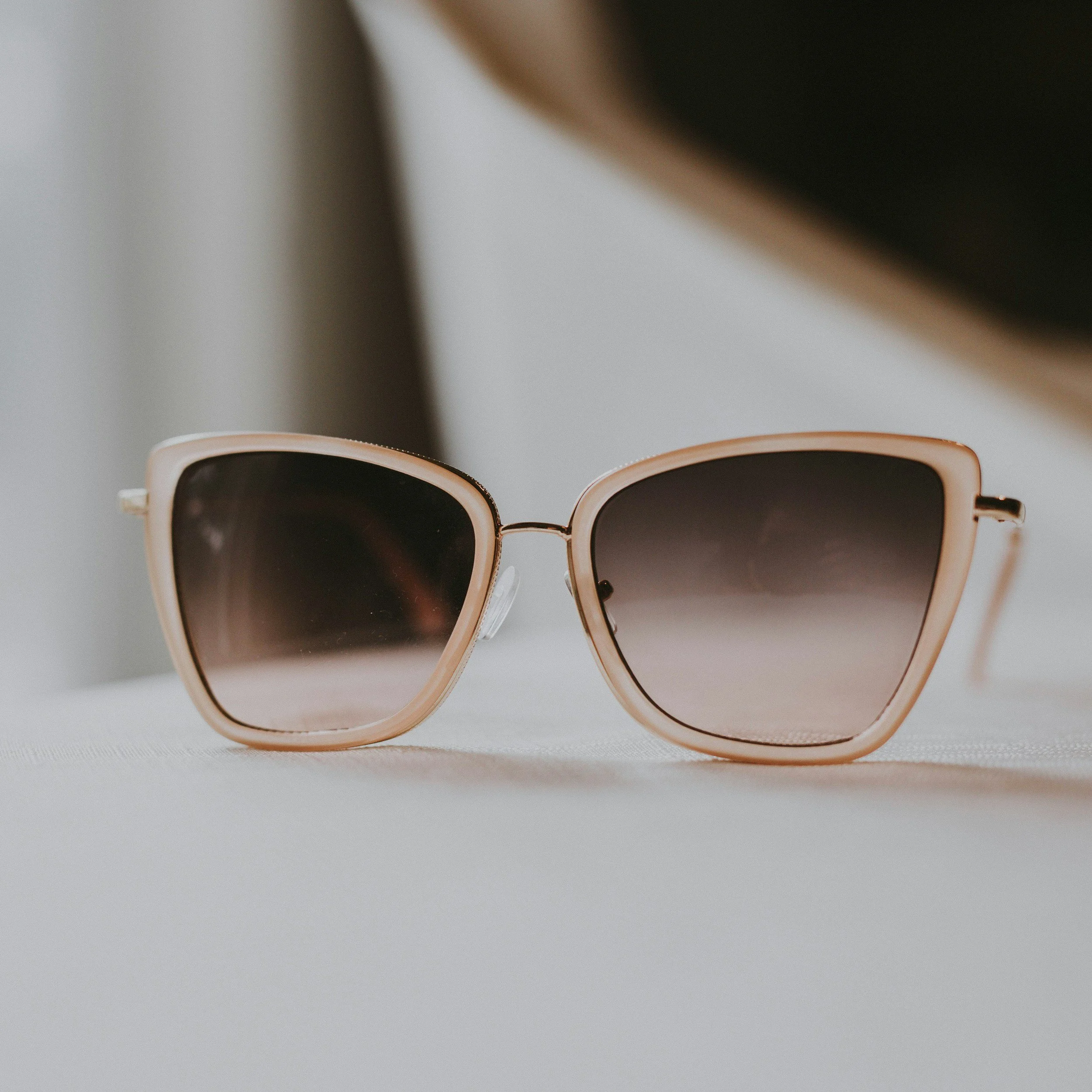 A pair of sunglasses with a rose gold frame and dark tinted lenses resting on a white surface.