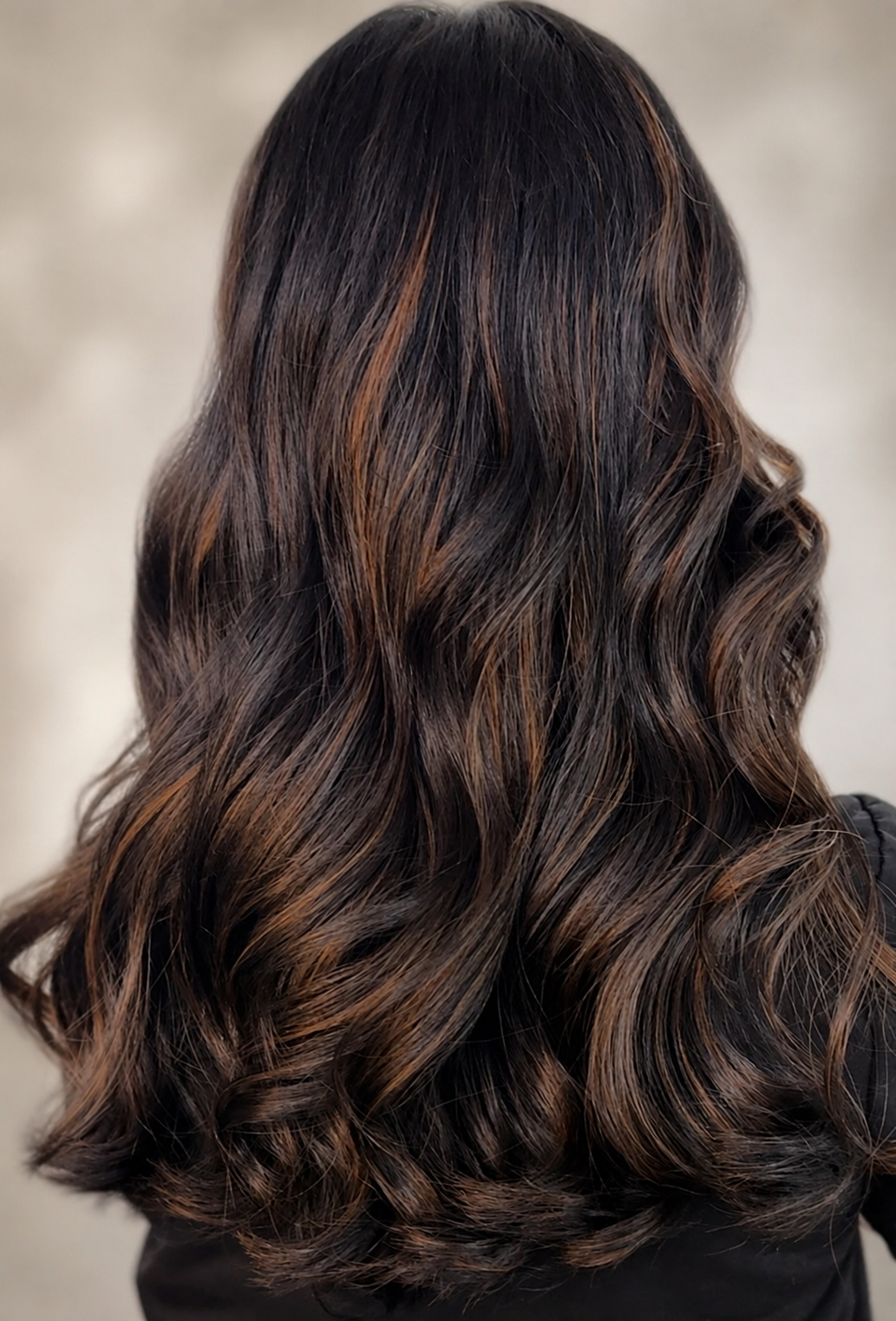 Back view of a person's head with medium-length wavy dark brown hair with lighter brown highlights.