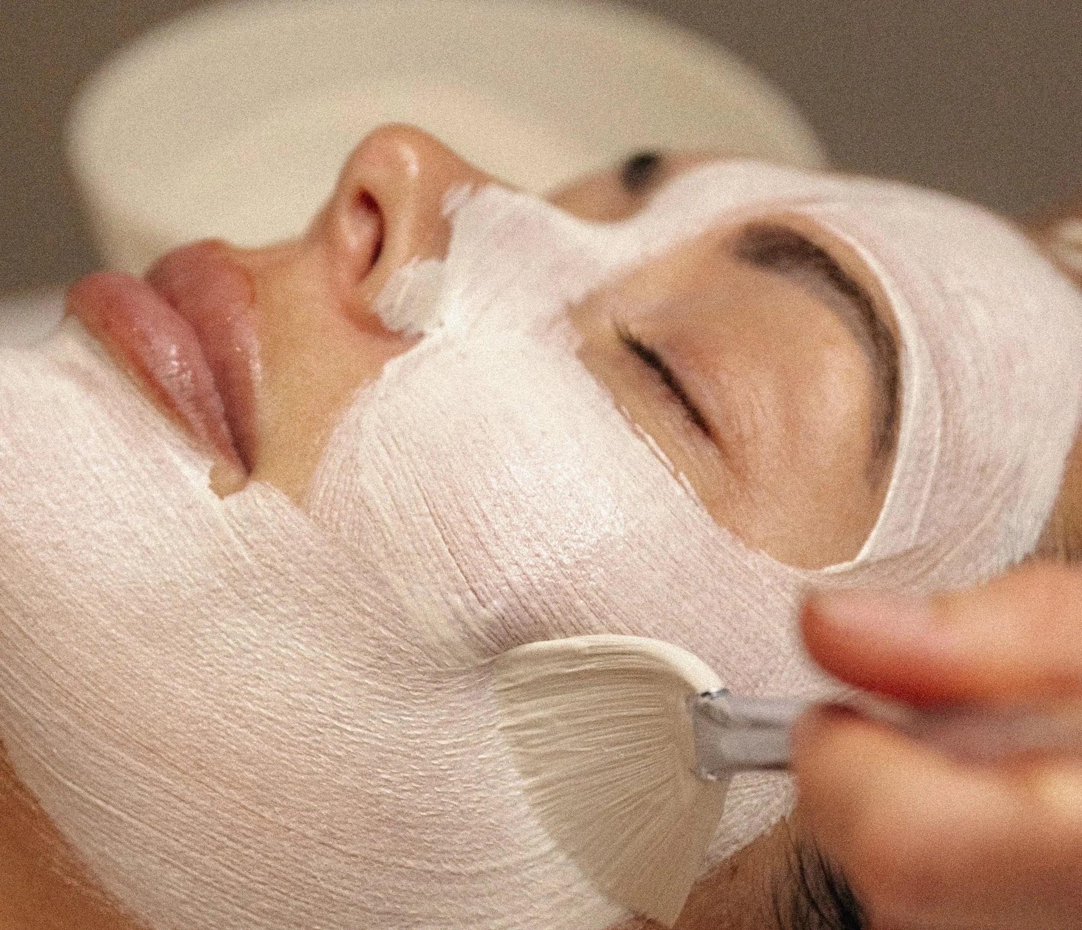 Close-up of a person's face with a bandage wrapped around the forehead and eye area, lying on a textured surface, with a hand holding a pen nearby.