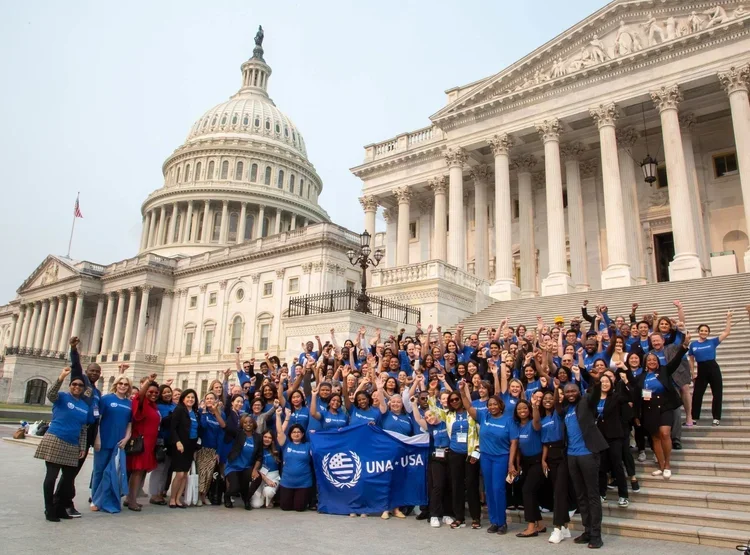 Group of people in blue shirts gathered on the steps of the U.S. Capitol building, holding UNA-USA banners and waving.