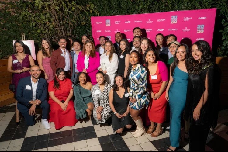Group of diverse people posing for a photo at the 50/50 event, with a pink backdrop displaying logos and sponsors.
