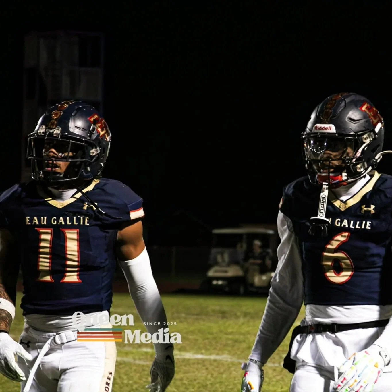 Two football players from Eau Gallie high school, wearing navy blue jerseys with white and red accents, standing on a football field at night.