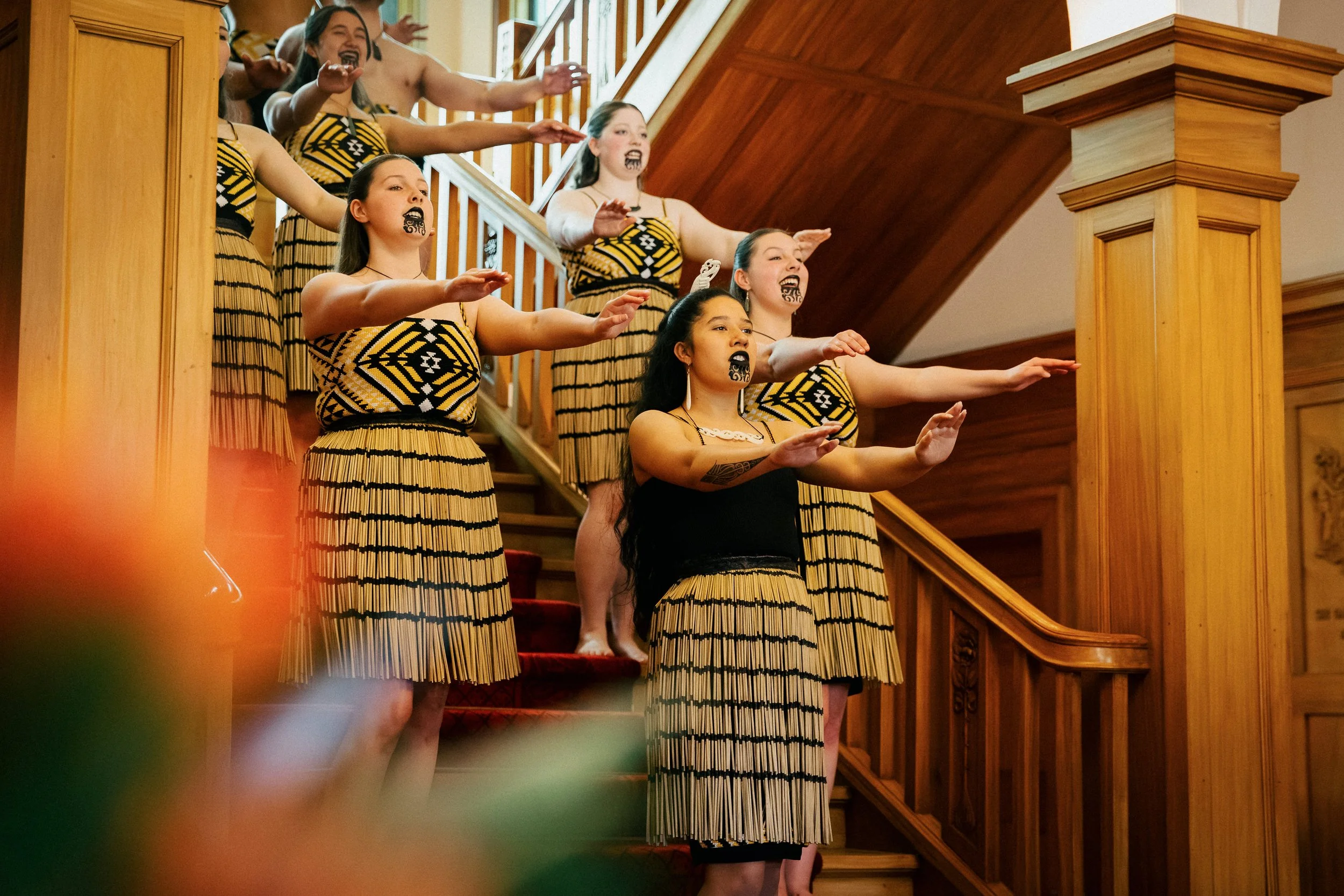 A group of women dressed in traditional Maori attire performing a Kapa Haka on a wooden staircase inside the Government House in Wellington, for the arrival of guests.